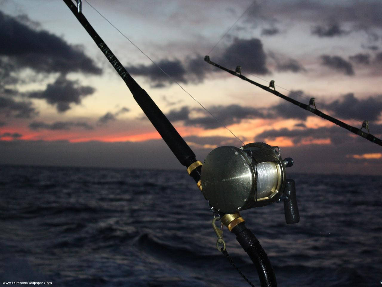 釣魚 桌布 壁紙 — 釣魚竿和捲線器在海洋上戲劇性的日落背景下形成剪影，天空有烏雲和橙色地平線。