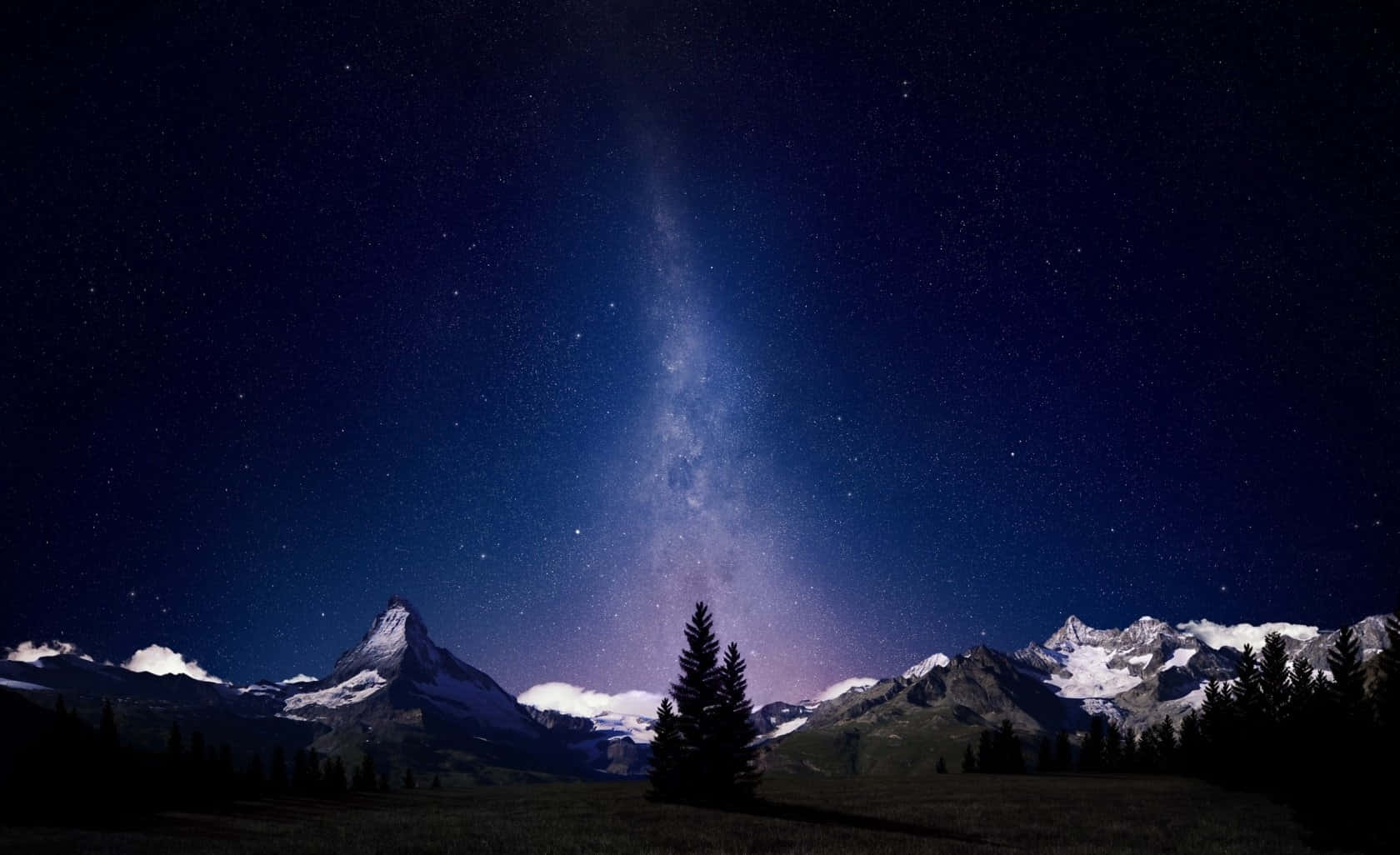 桌布 壁紙 — 銀河在積雪的山峰上燦爛地彎曲，星空下松樹的剪影清晰可見。