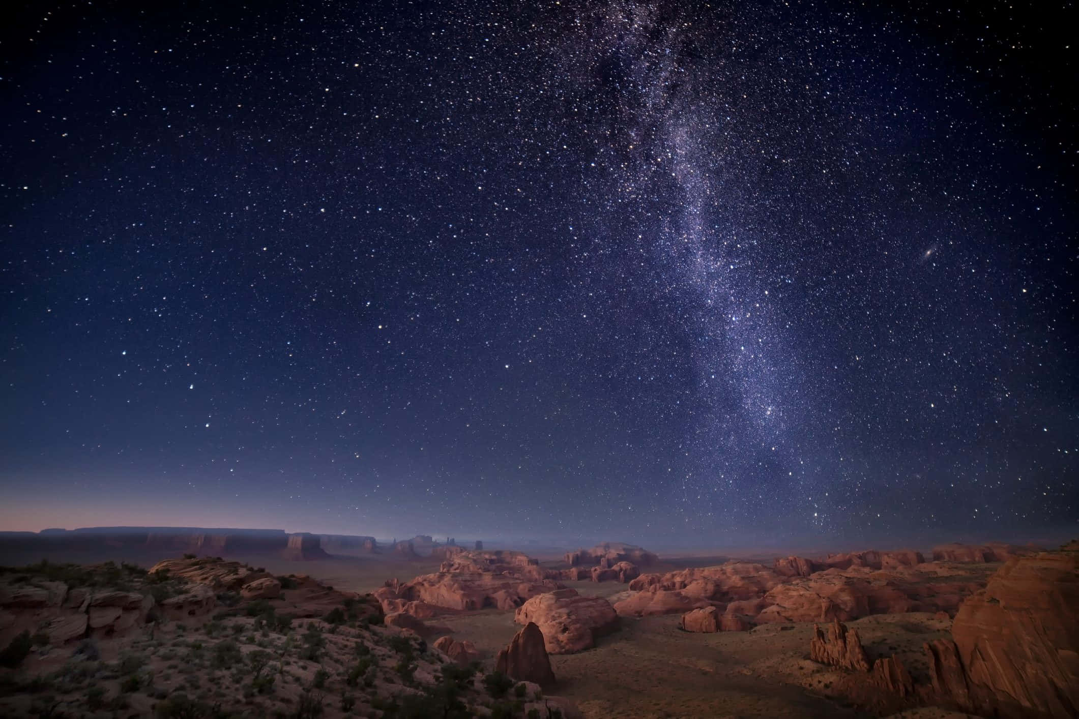 Stars 桌布 壁紙 — 銀河系在夜晚燦爛地拱起於沙漠峽谷之上，下方是發光的紅色岩層。