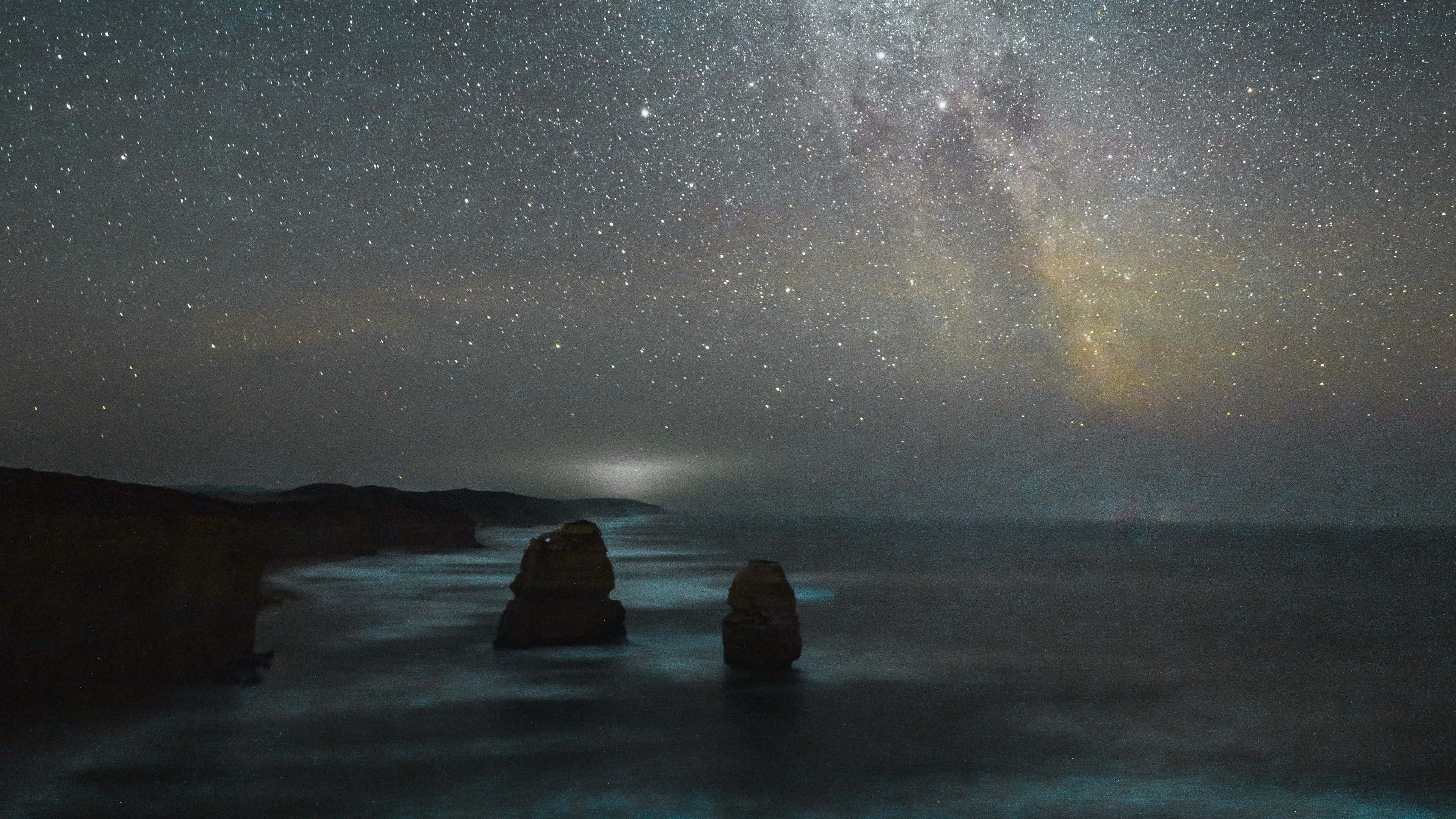 桌布 壁紙 — 銀河系在星空下彎曲於兩個海蝕柱之上，下方是平靜的海水。