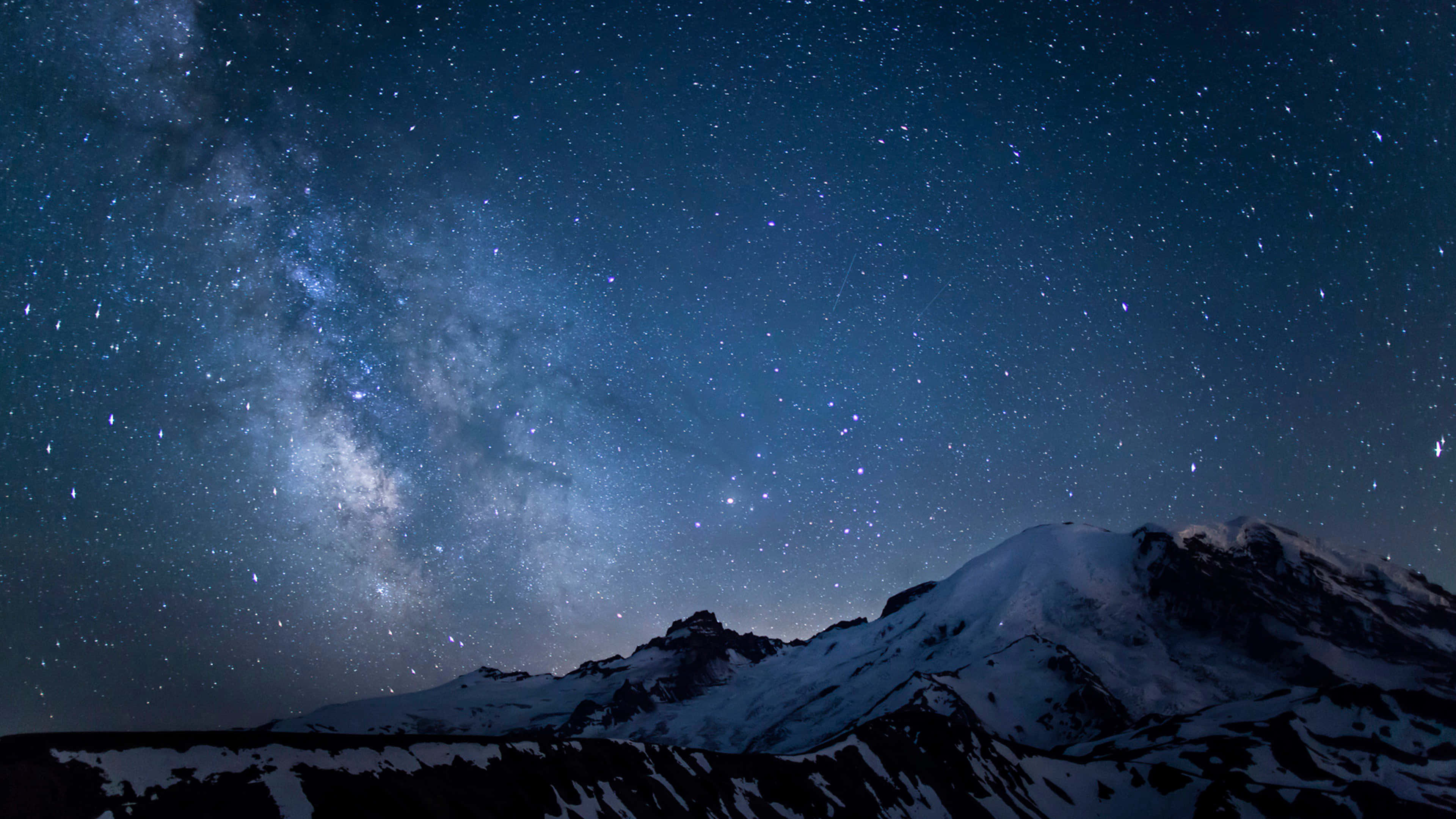 Starry 桌布 壁紙 — 銀河系在深藍色星空下，燦爛地拱起在積雪的山脈之上。