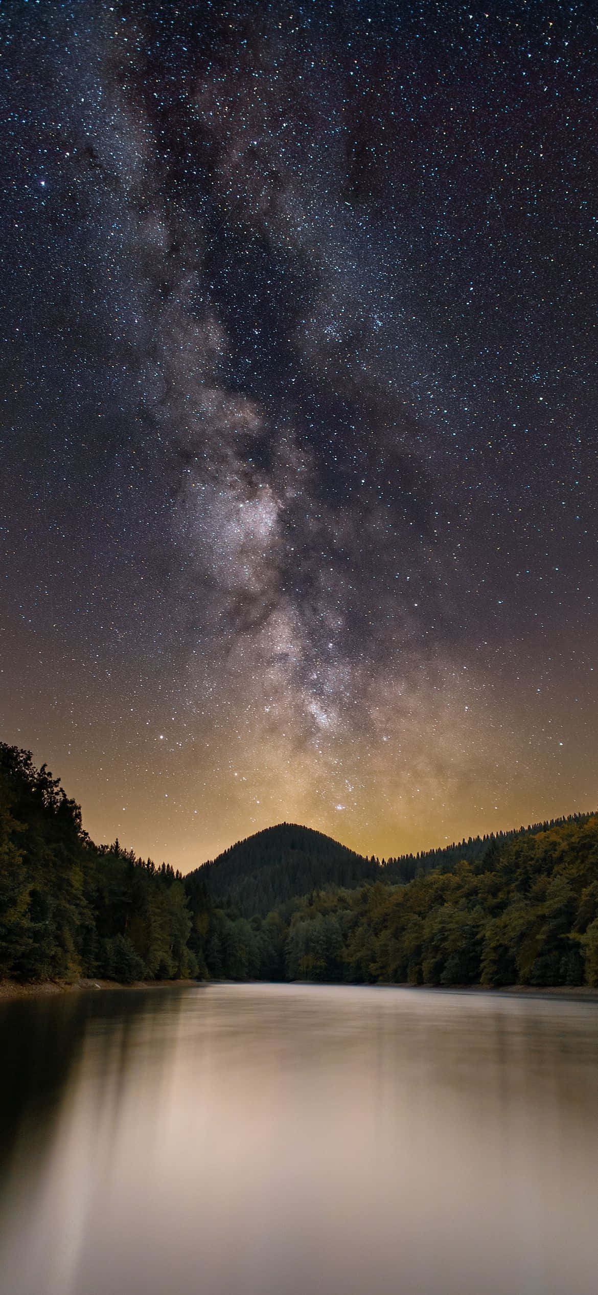 桌布 壁紙 — 銀河系在深邃夜空下，於寧靜的湖面上方彎曲，湖面映照著星星和森林覆蓋的山丘。