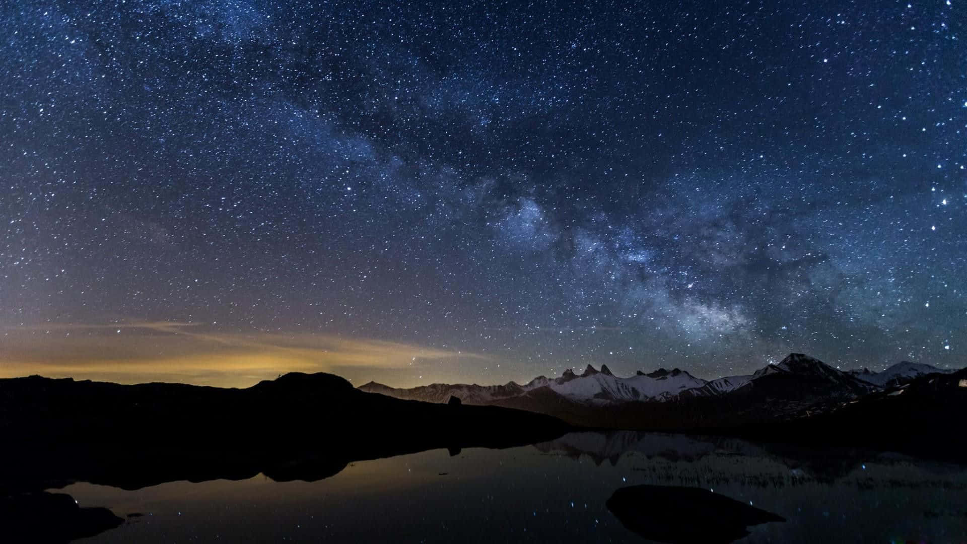 Chilly Night 桌布 壁紙 — 銀河系在積雪的山峰上空彎曲，倒映在寧靜的高山湖泊中，星空璀璨。