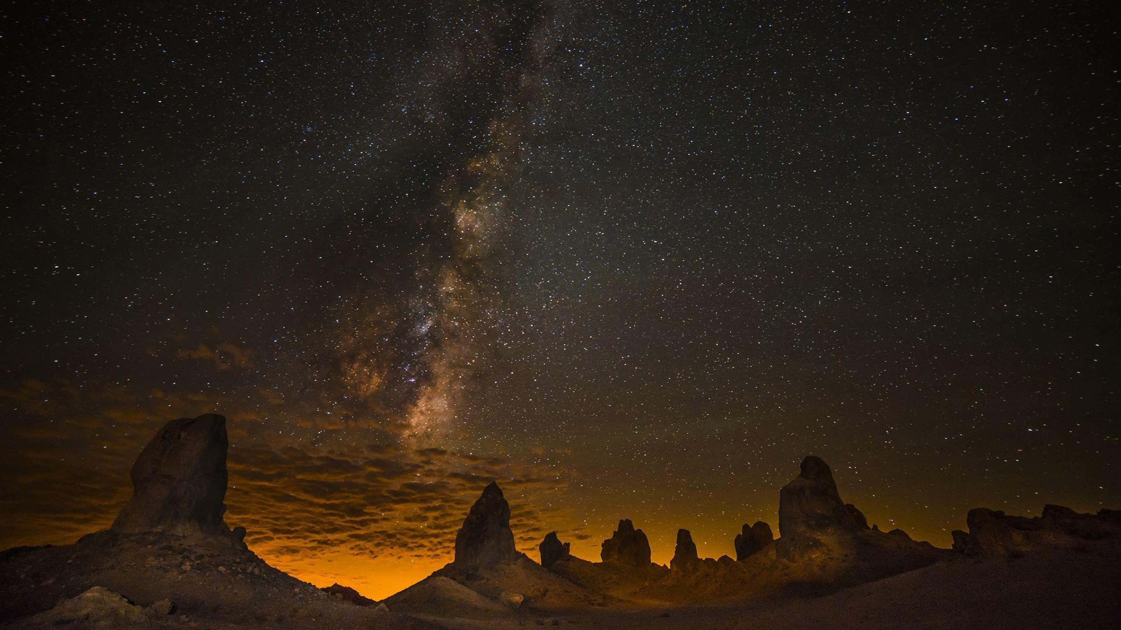Silhouette 桌布 壁紙 — 銀河系在繁星點點的夜空下，在崎嶇的沙漠岩石層上燦爛地彎曲。