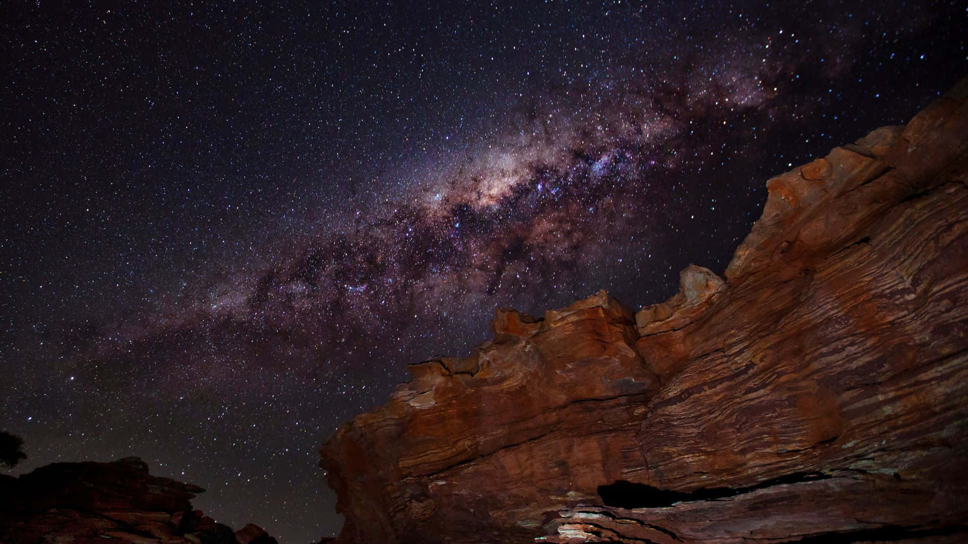 黑夜 桌布 壁紙 — 銀河系在繁星點點的夜空下，在崎嶇的紅色岩層上燦爛地彎曲。