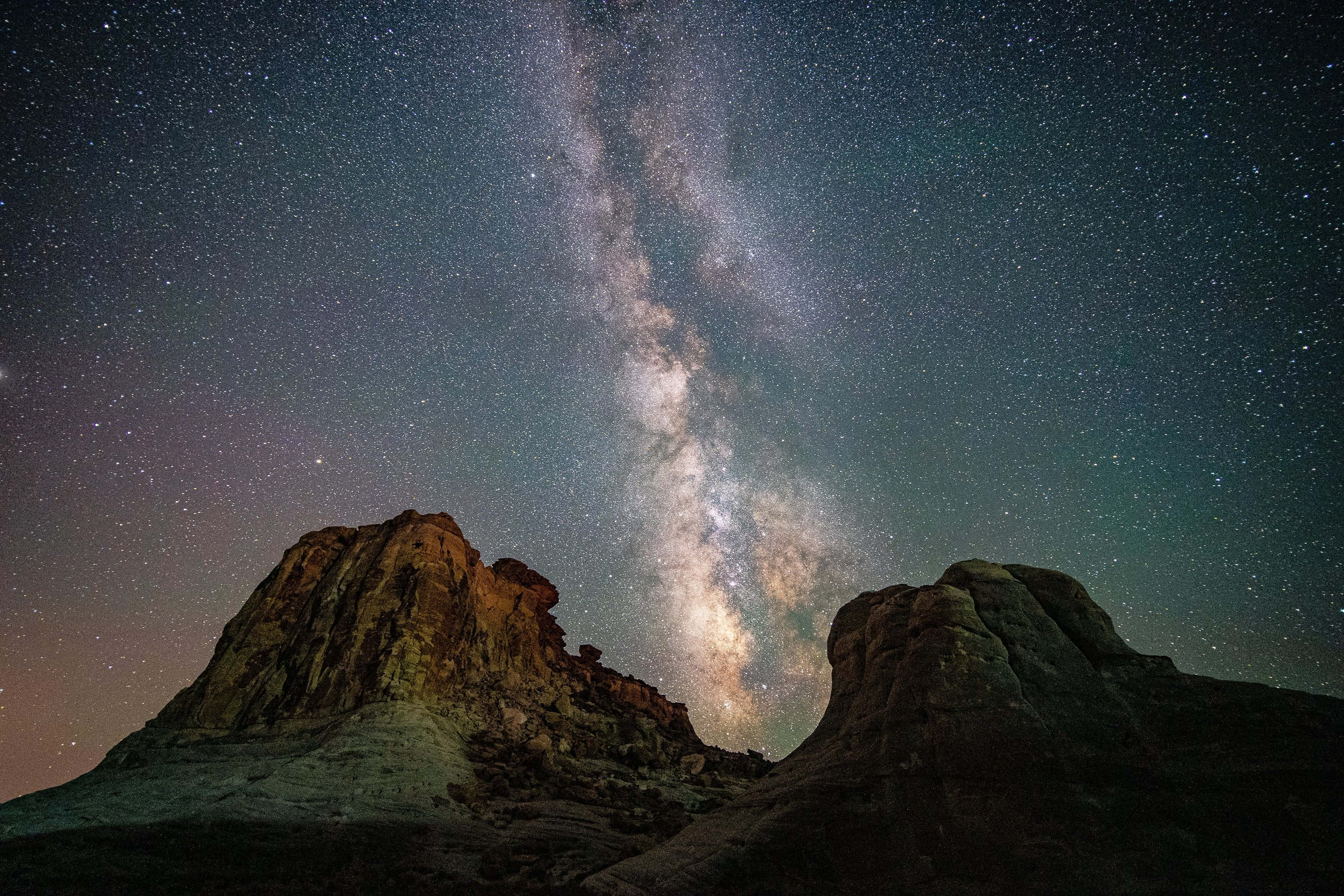 Star Sky 桌布 壁紙 — 銀河系在繁星點點的夜空下，壯麗地拱起於崎嶇的沙漠岩石地貌之上。