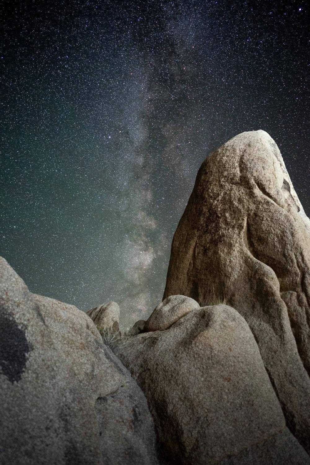 銀河 桌布 壁紙 — 銀河系在繁星點點的夜空下，彎曲在崎嶇的沙漠岩石層之上。