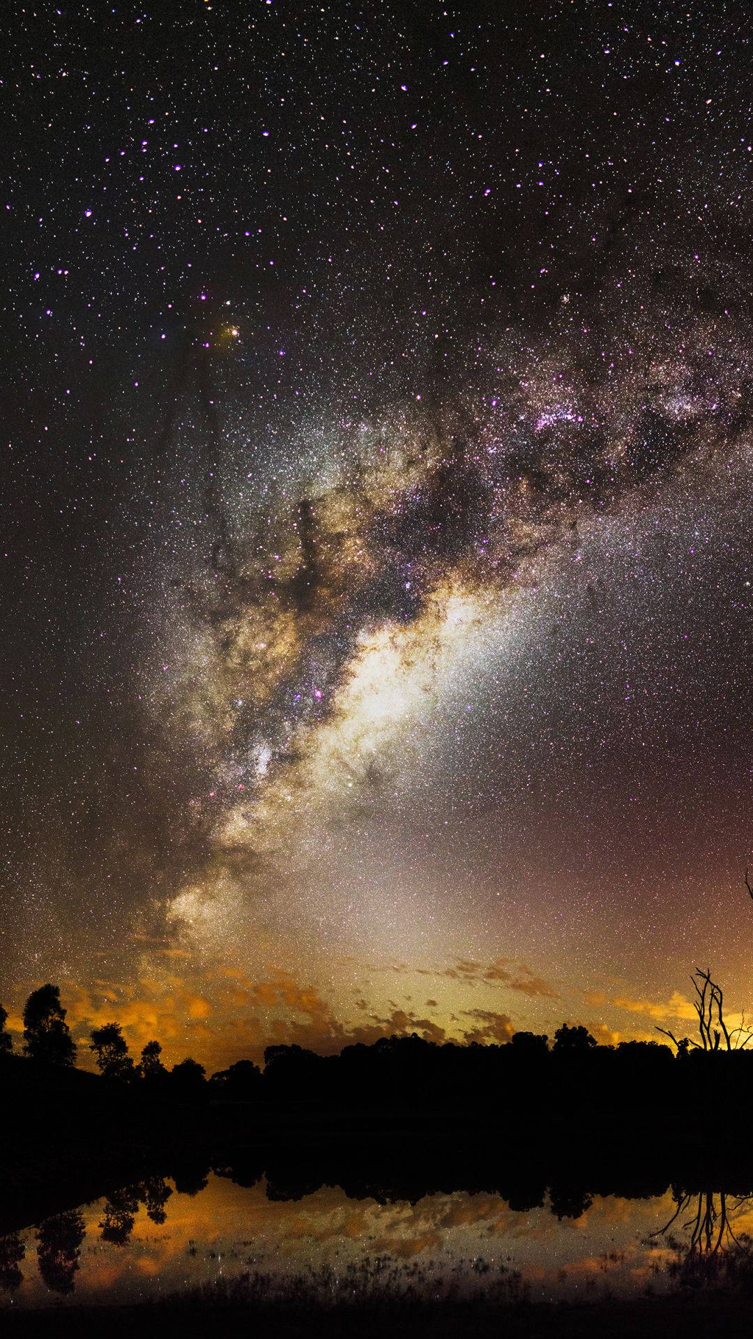 Milky 桌布 壁紙 — 銀河系在繁星點點的夜空中劃過一道弧線，下方是剪影般的樹線和反射的水面。