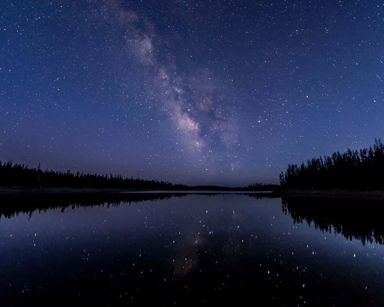 Starry Sky 桌布 壁紙 — 銀河系橫跨繁星點點的夜空，完美倒映在黑暗森林環繞的平靜湖面上。