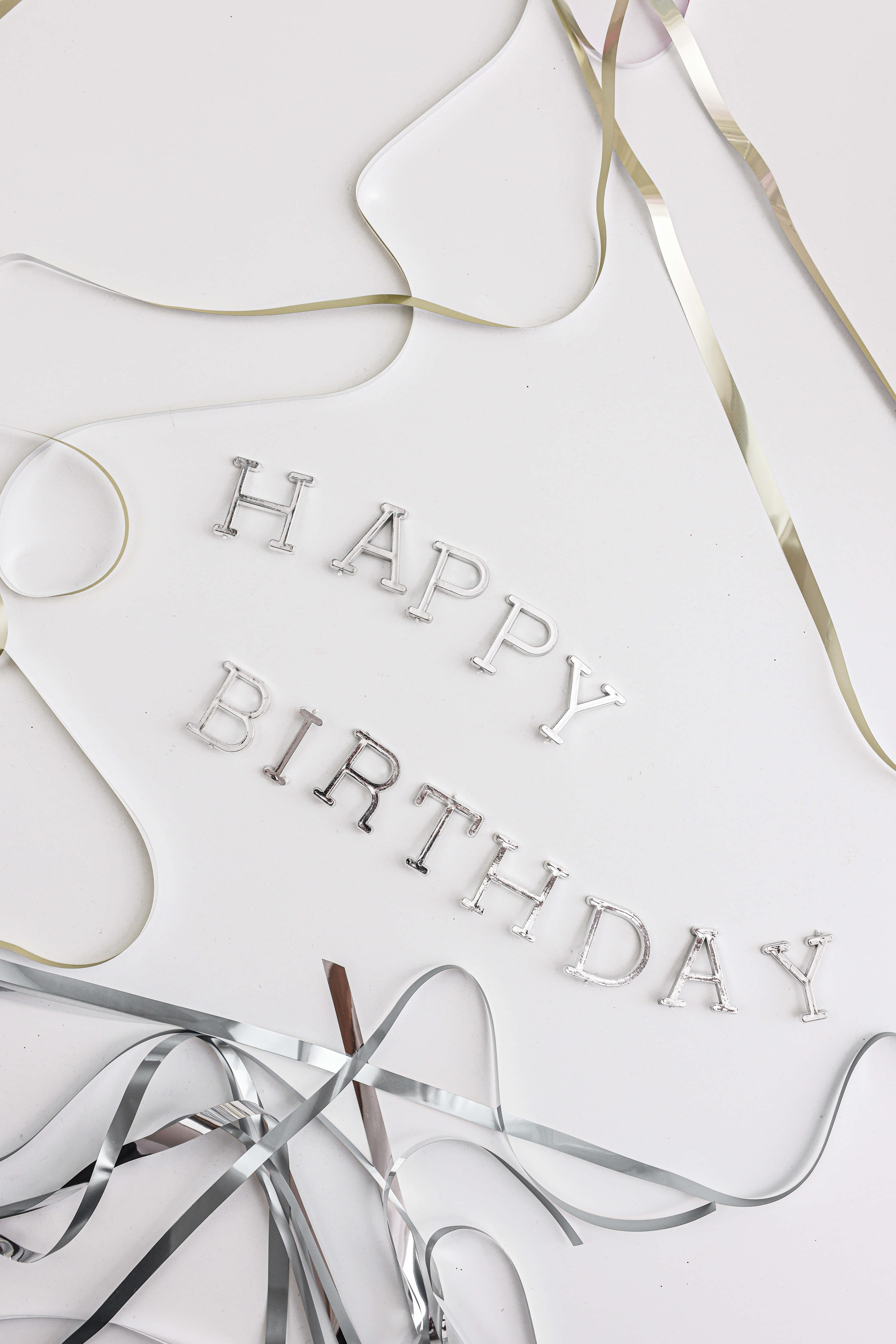 Cute Birthday 桌布 壁紙 — 銀色 'HAPPY BIRTHDAY' 字母和金屬絲帶散落在潔白的表面上。
