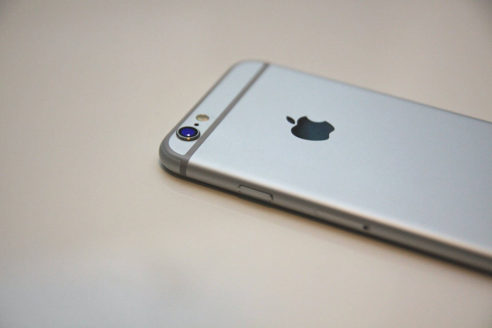 original iPhone 6 桌布 壁紙 — 銀色 iPhone 6s 的特寫，Apple 標誌和相機鏡頭在純色米白色表面上。