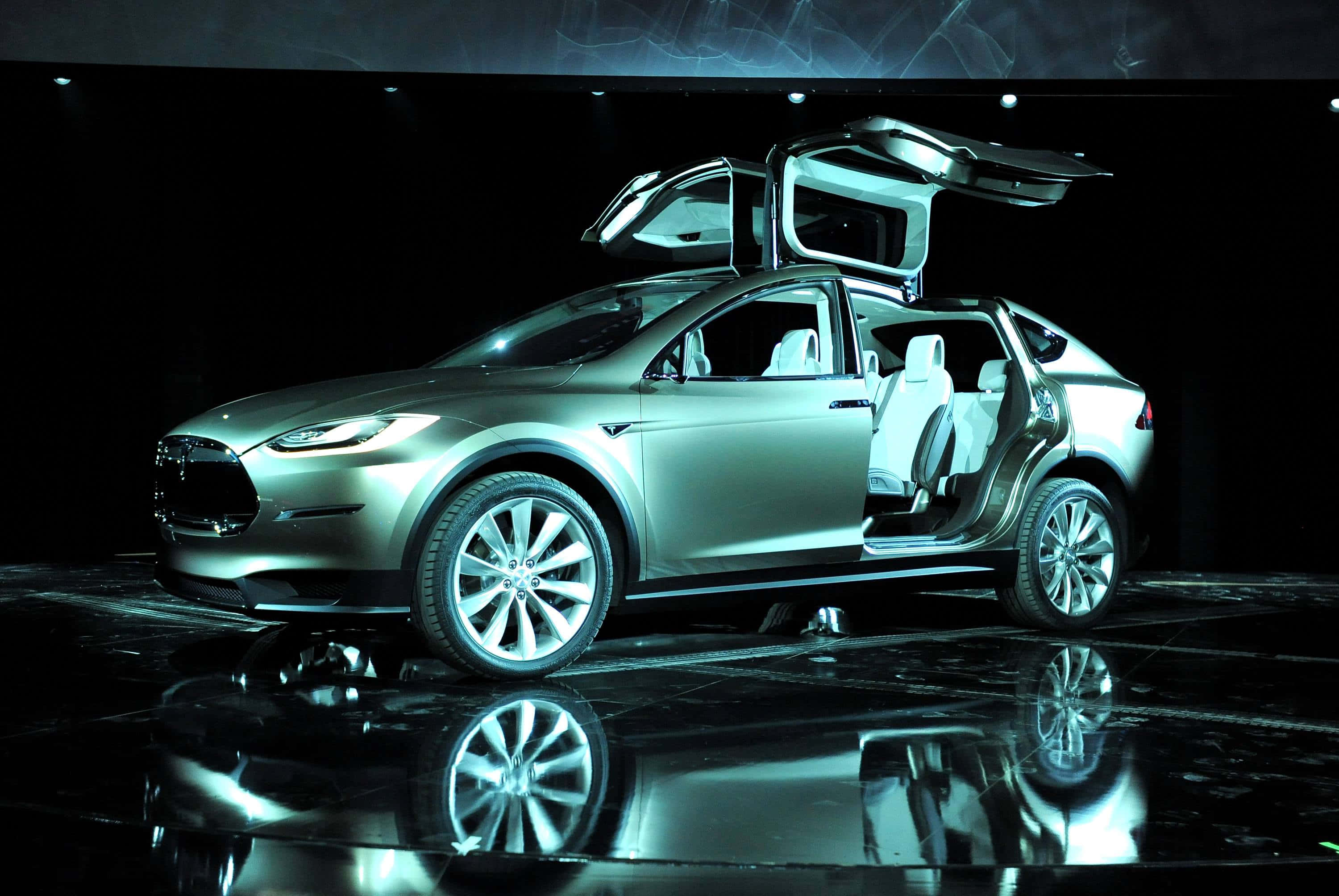 特斯拉 桌布 壁紙 — 銀色 Tesla Model X，鷹翼門打開，在戲劇性的藍色燈光下於光澤舞台上展示。