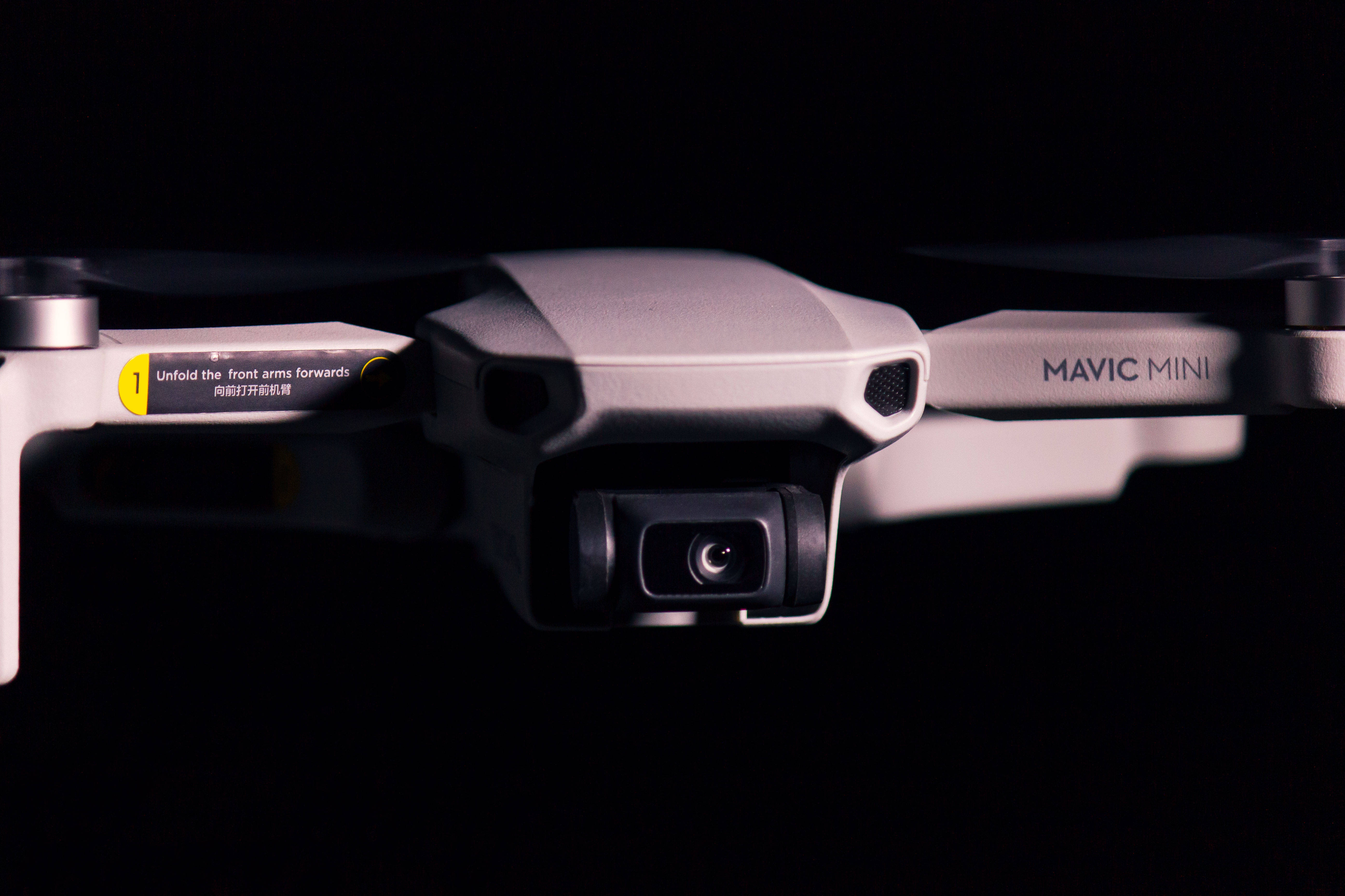 網路攝影機 桌布 壁紙 — 銀色DJI Mavic Mini無人機特寫，黑色背景，可見相機和手臂指示。