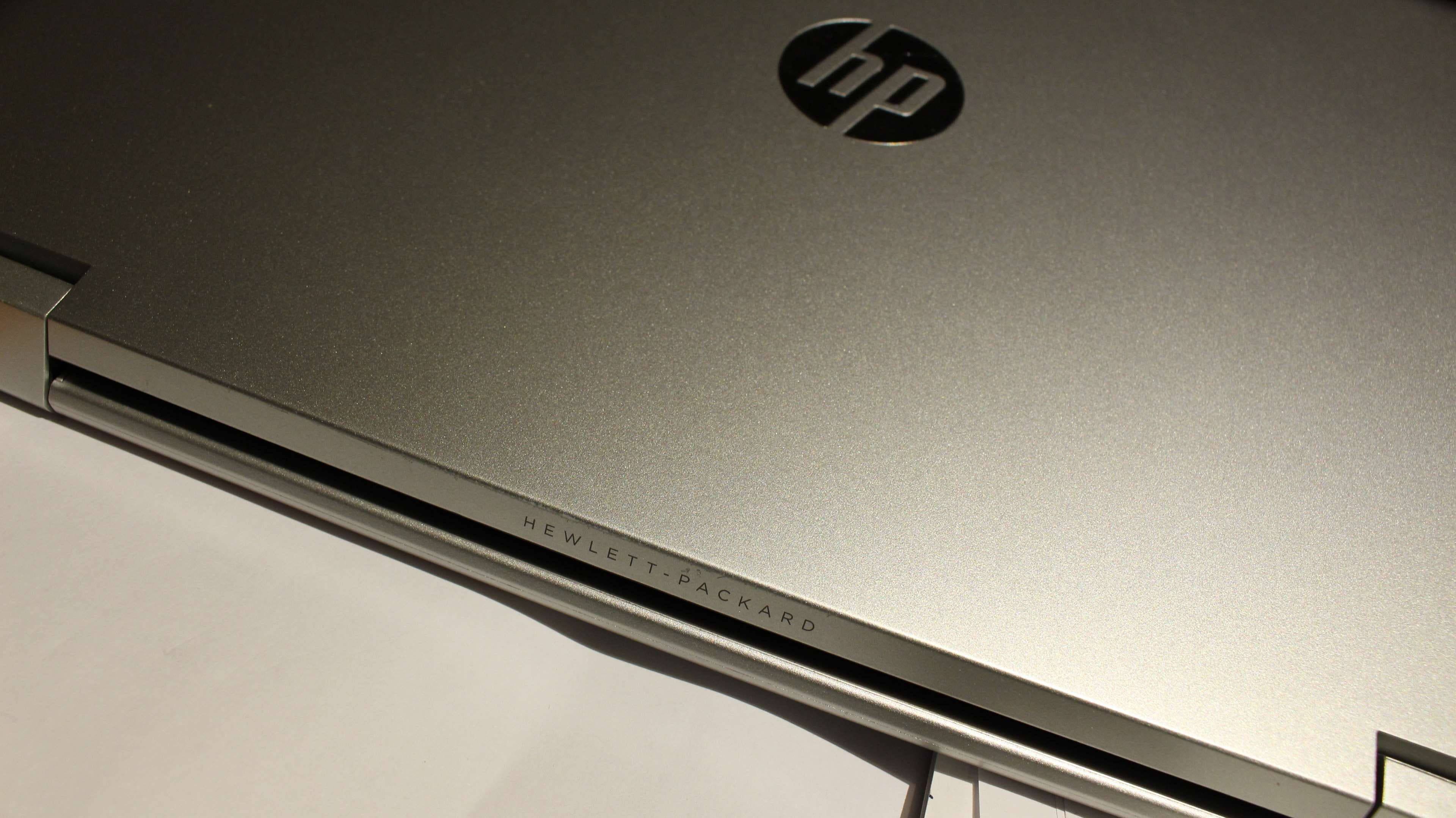 Hp Laptop 桌布 壁紙 — 銀色HP筆記型電腦蓋的特寫，在柔和燈光下顯示標誌和Hewlett-Packard雕刻。