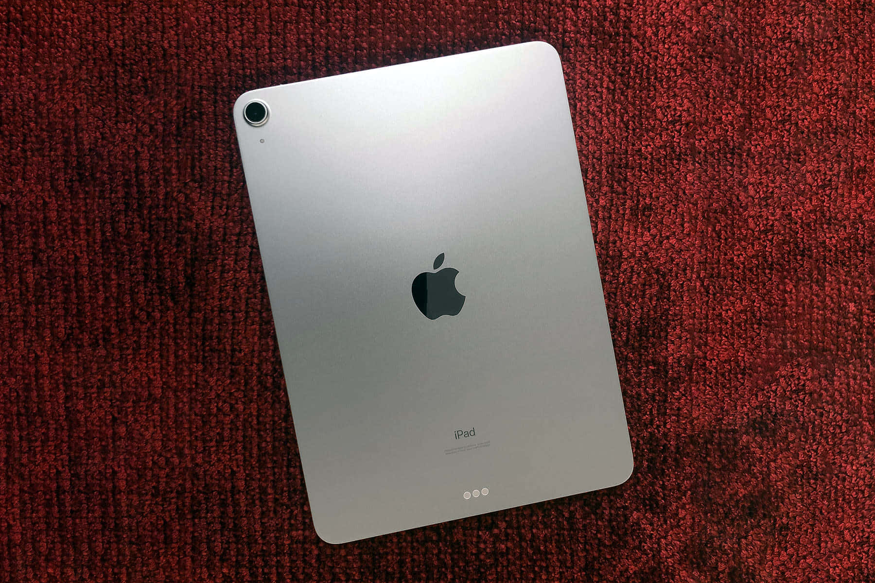 iPad 桌布 壁紙 — 銀色iPad對角放置在質感豐富的紅色地毯上，帶有柔和環境光線。
