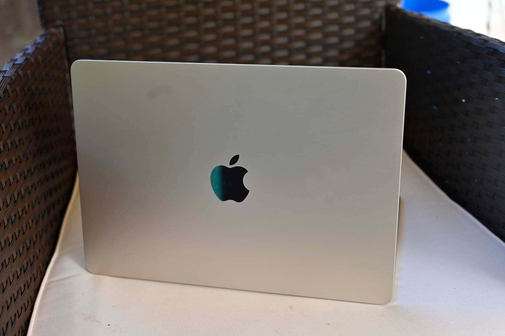 MacBook 動態圖片 桌布 壁紙 — 銀色MacBook蓋上帶有Apple標誌，放在戶外白色軟墊柳條椅上。