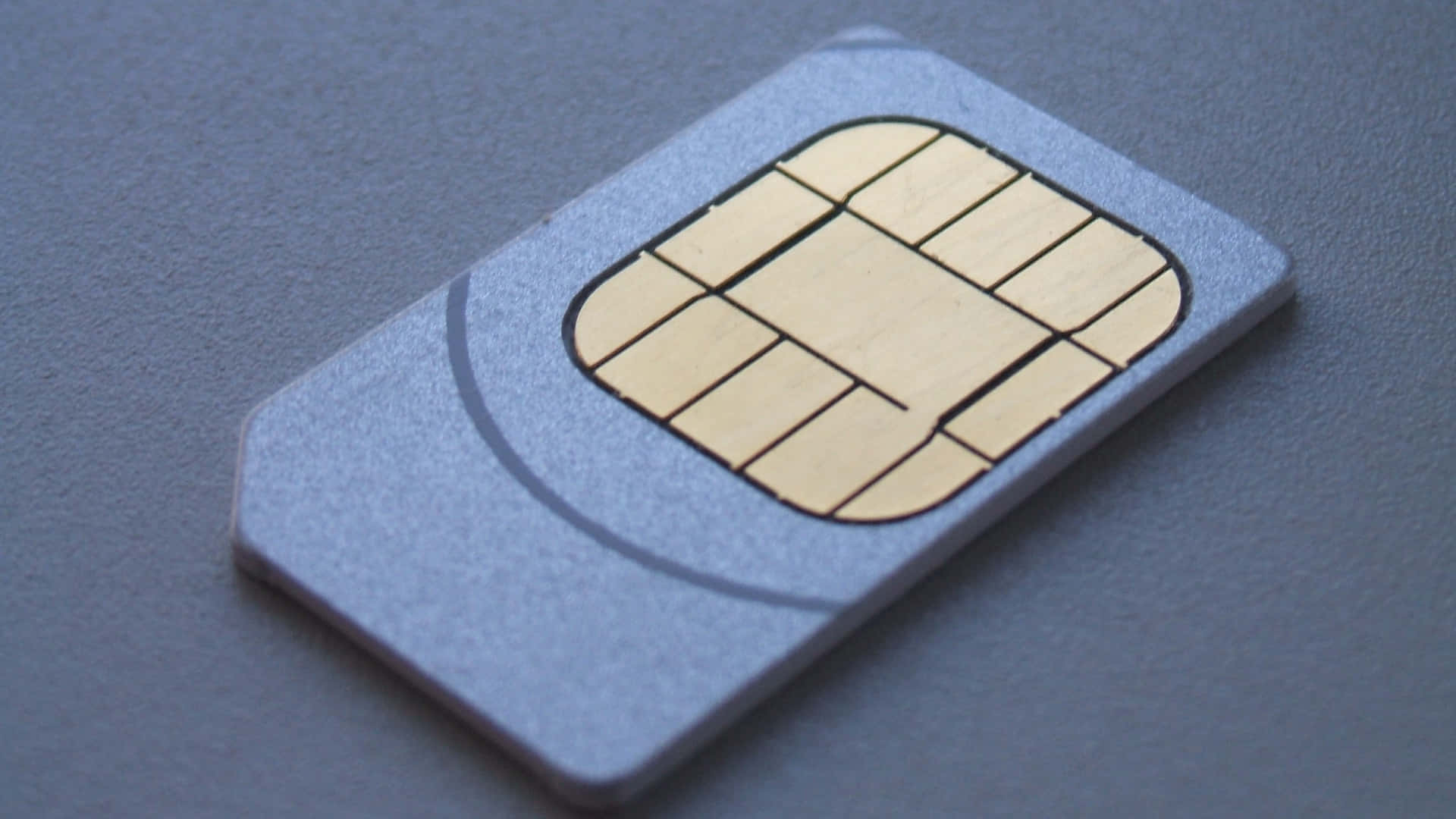 Sim Card-2. 壁紙 — 銀色SIM卡帶金色接觸點，置於紋理灰色表面上的特寫。