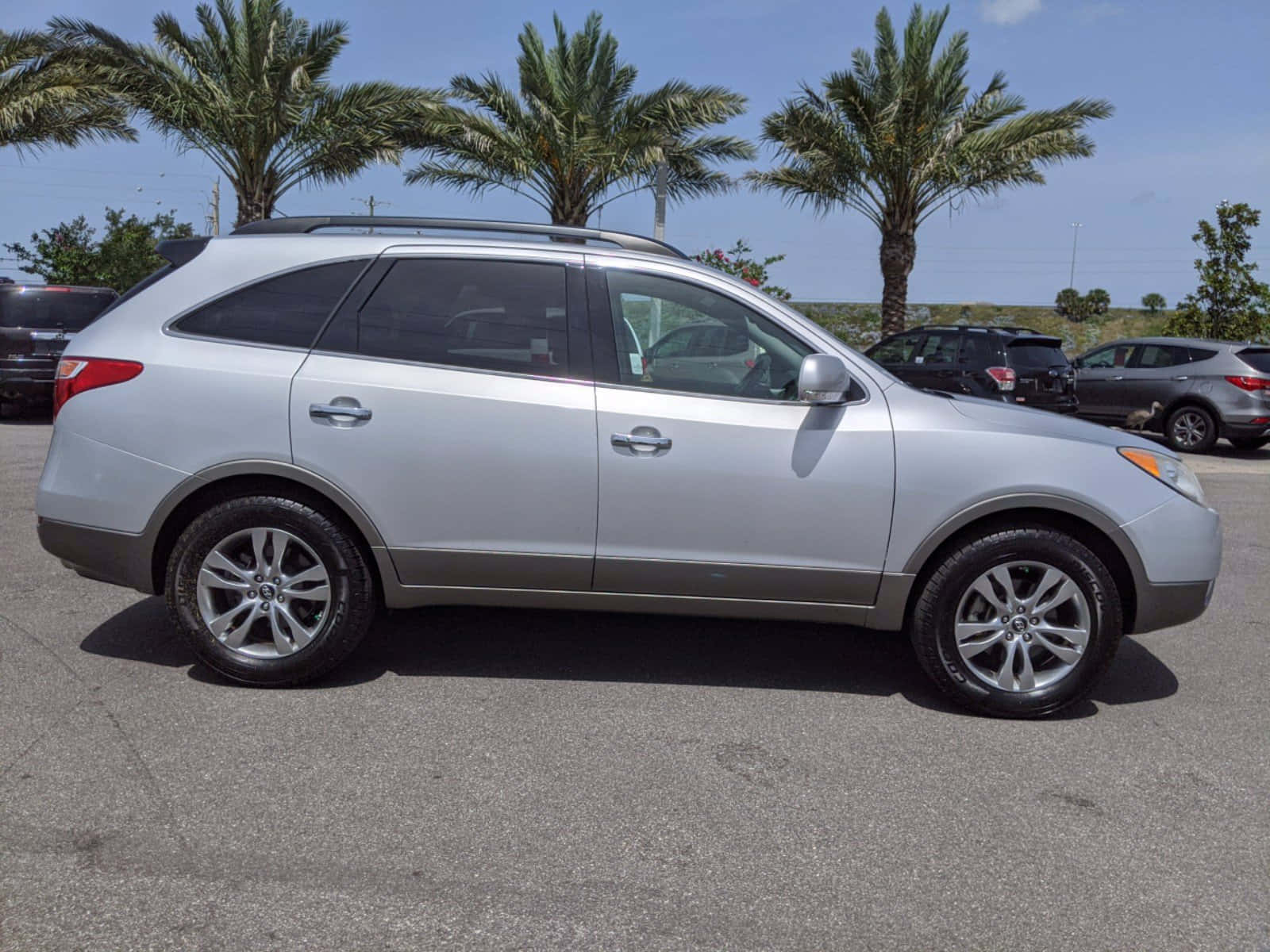 Hyundai Veracruz 桌布 壁紙 — 銀色SUV停放在陽光明媚的停車場，背景有棕櫚樹在清澈藍天下搖曳。