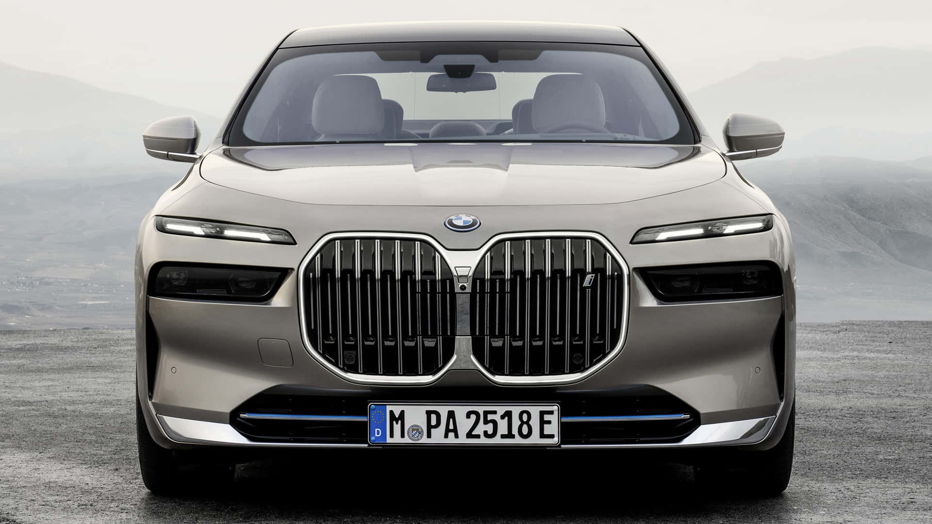 BMW 動圖 桌布 壁紙 — 銀色寶馬電動車的正面視圖，帶有標誌性腎形格柵，背景是霧濛濛的山巒。