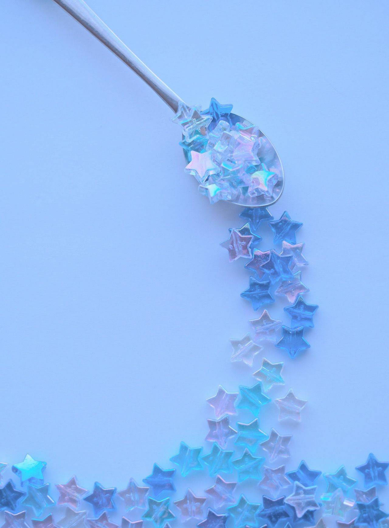 Blue Pastel Aesthetic 桌布 壁紙 — 銀色湯匙在柔和的粉藍色背景上倒出閃爍藍色星形紙屑。