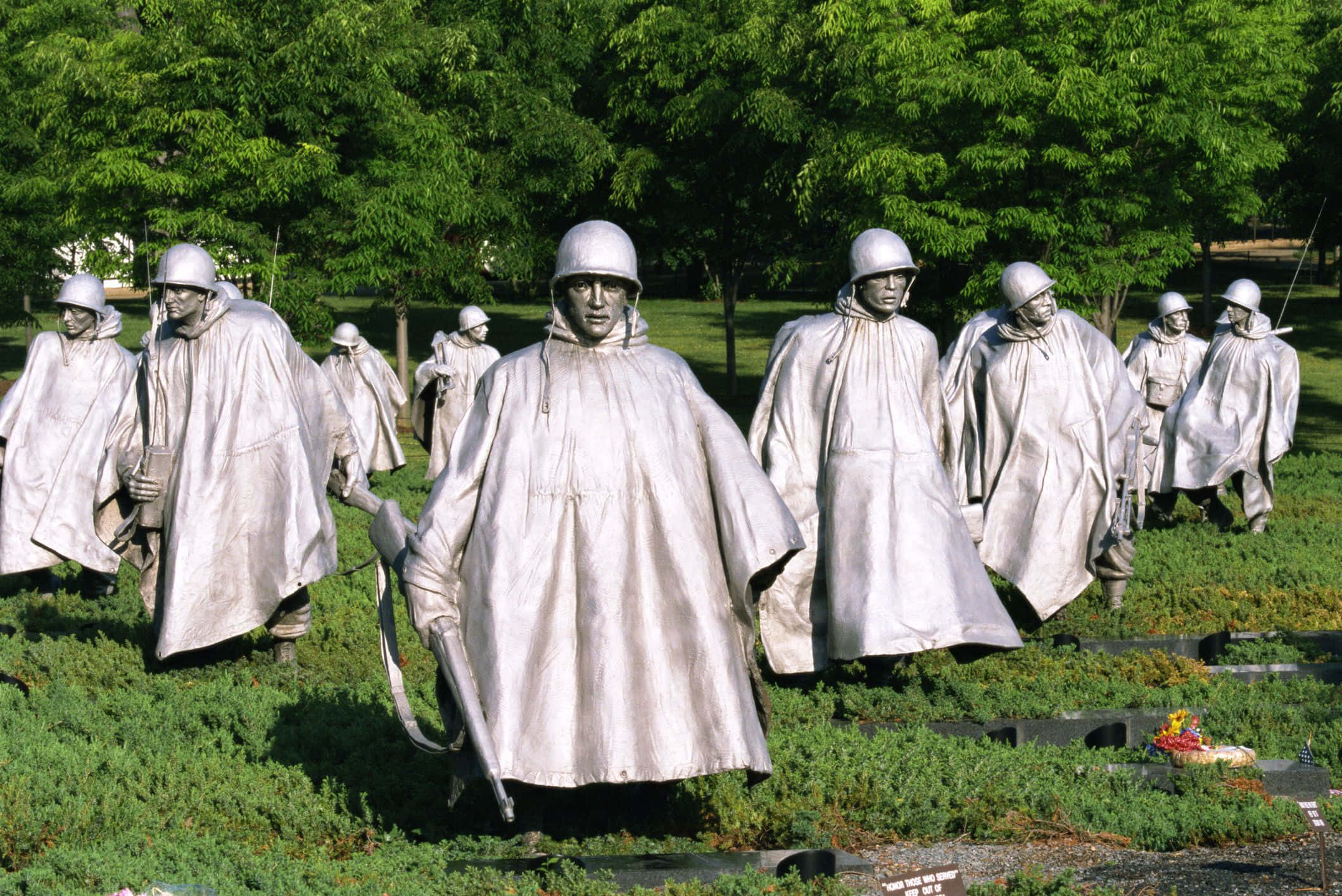 Memorial 桌布 壁紙 — 銀色的士兵雕像穿著斗篷和頭盔，在明亮的綠樹下的草地上行進。