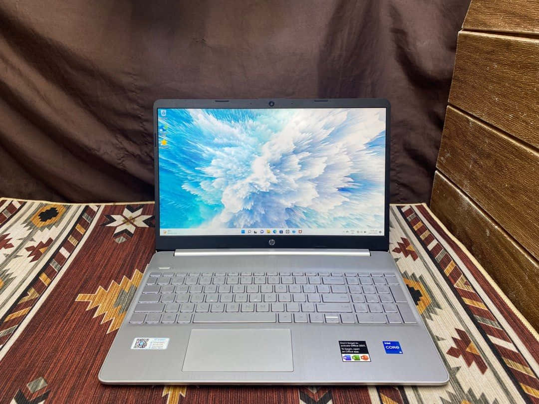 HP 桌布 壁紙 — 銀色筆記型電腦帶有雲端桌布，放在圖案地毯上，旁邊有木條和棕色布料。
