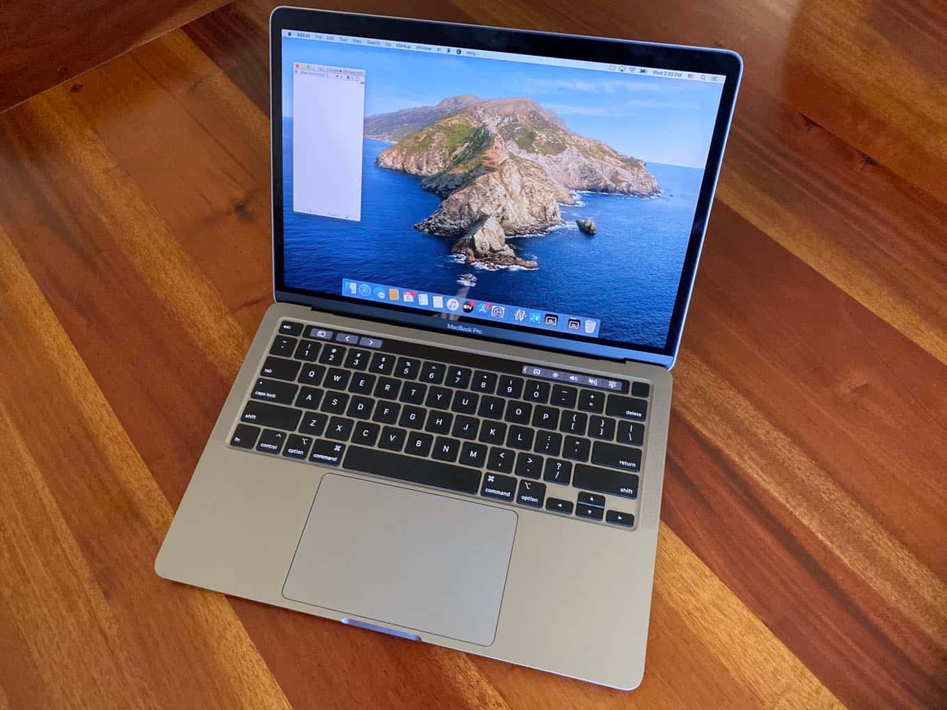 MacBook 動態圖片 桌布 壁紙 — 銀色筆記型電腦放在木桌上，顯示藍色海洋中晴朗天空下的岩石島嶼。