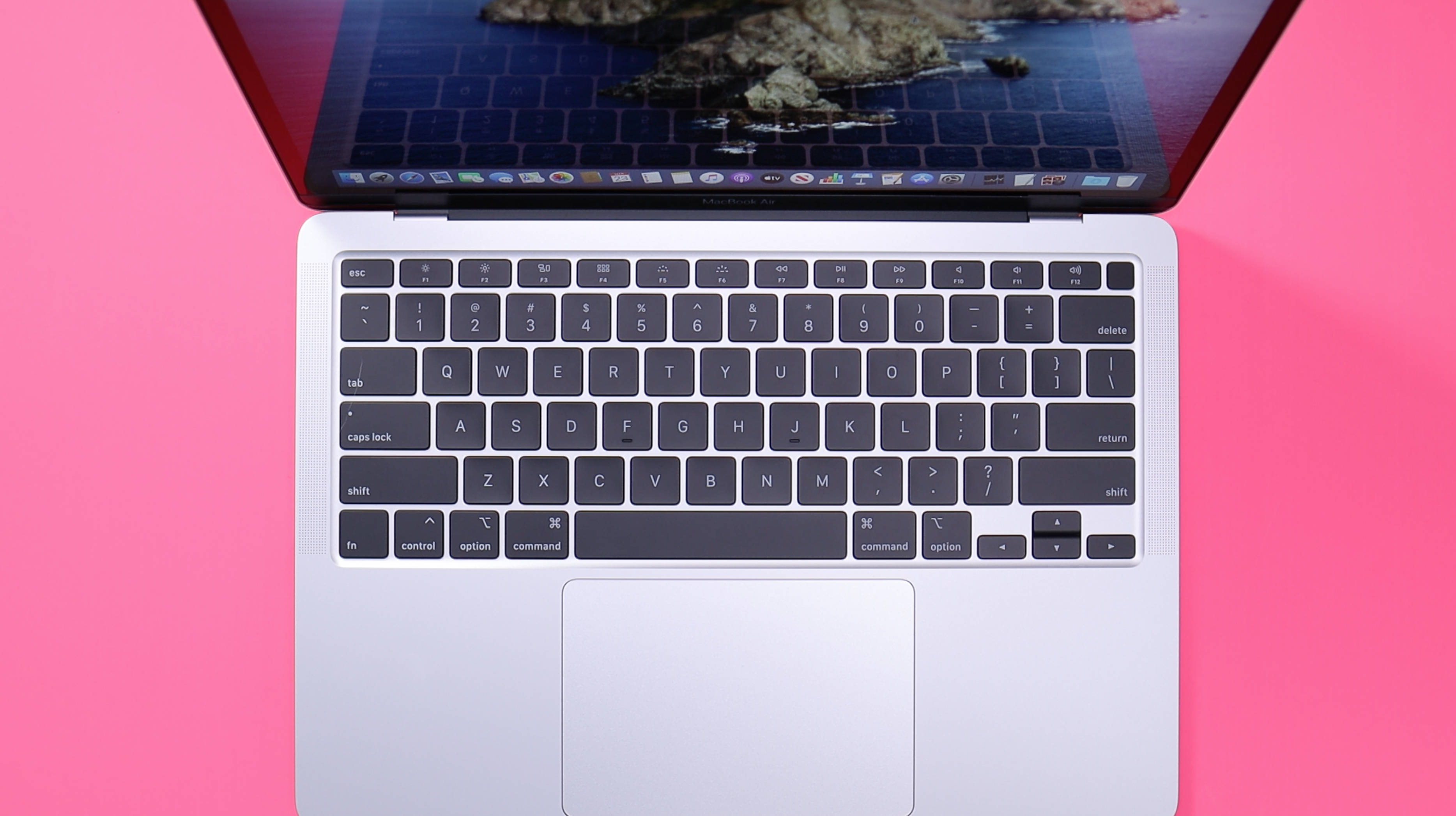 Macbook Air 2020 桌布 壁紙 — 銀色筆記型電腦配黑色鍵盤打開，放在鮮豔粉紅色背景上，顯示海洋桌布。