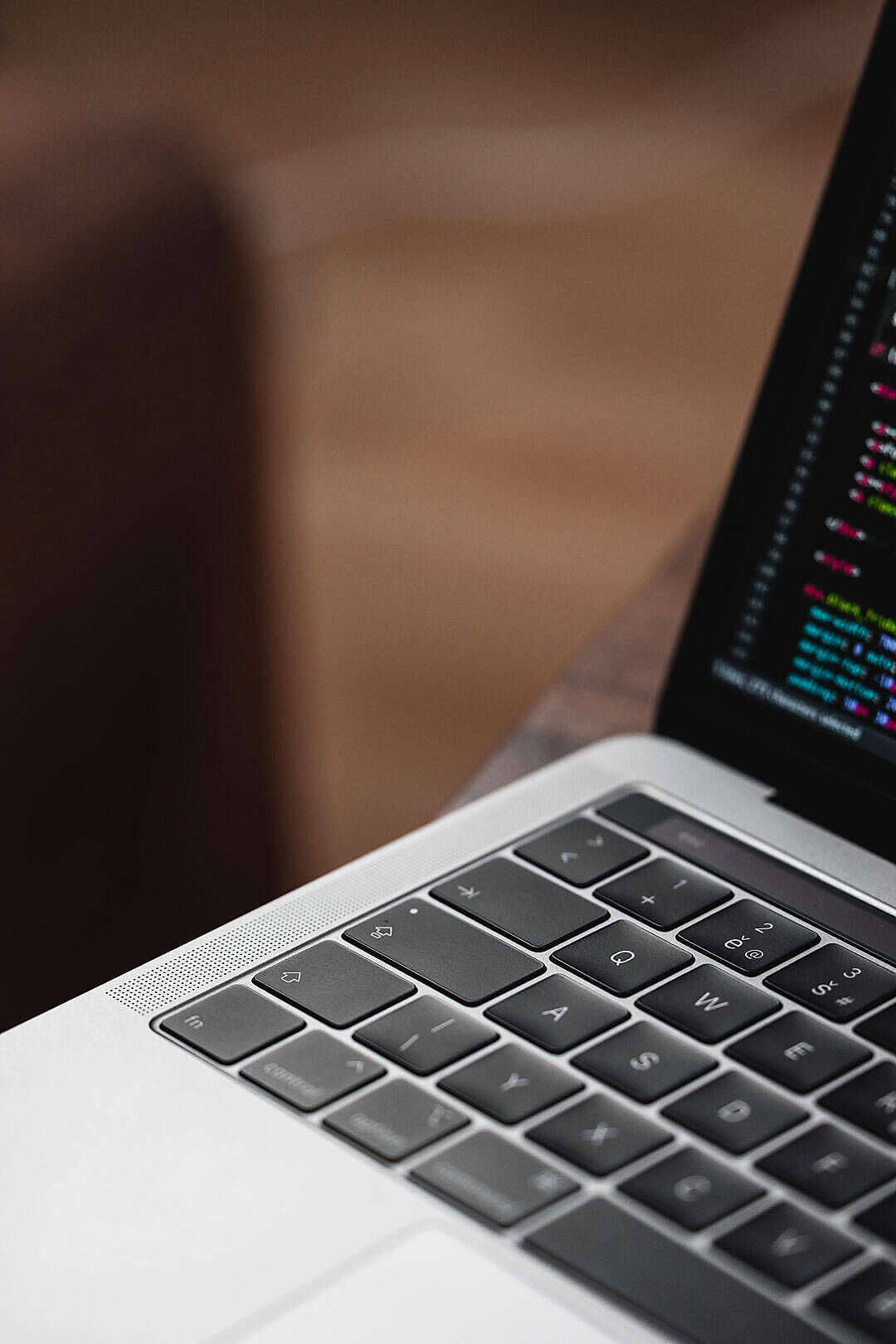 Macbook Air 2020 桌布 壁紙 — 銀色筆記型電腦鍵盤的特寫，螢幕上顯示彩色代碼滾動，背景為模糊的木質。