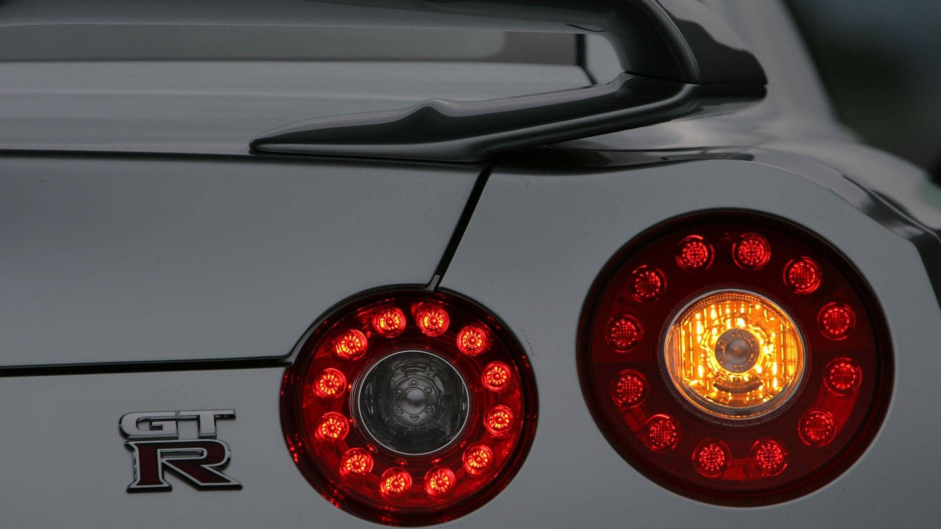 日產 桌布 壁紙 — 銀色跑車紅色和琥珀色圓形尾燈的特寫，帶有'GT-R'徽章。