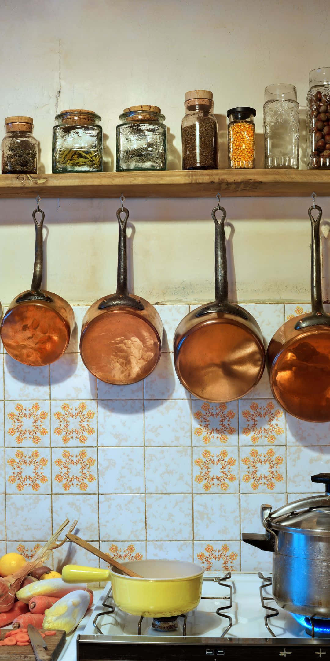 Pixel 3 Kitchen 桌布 壁紙 — 銅鍋掛在香料罐架下方，瓷磚廚房牆上方，有燃燒的爐灶和新鮮蔬菜。