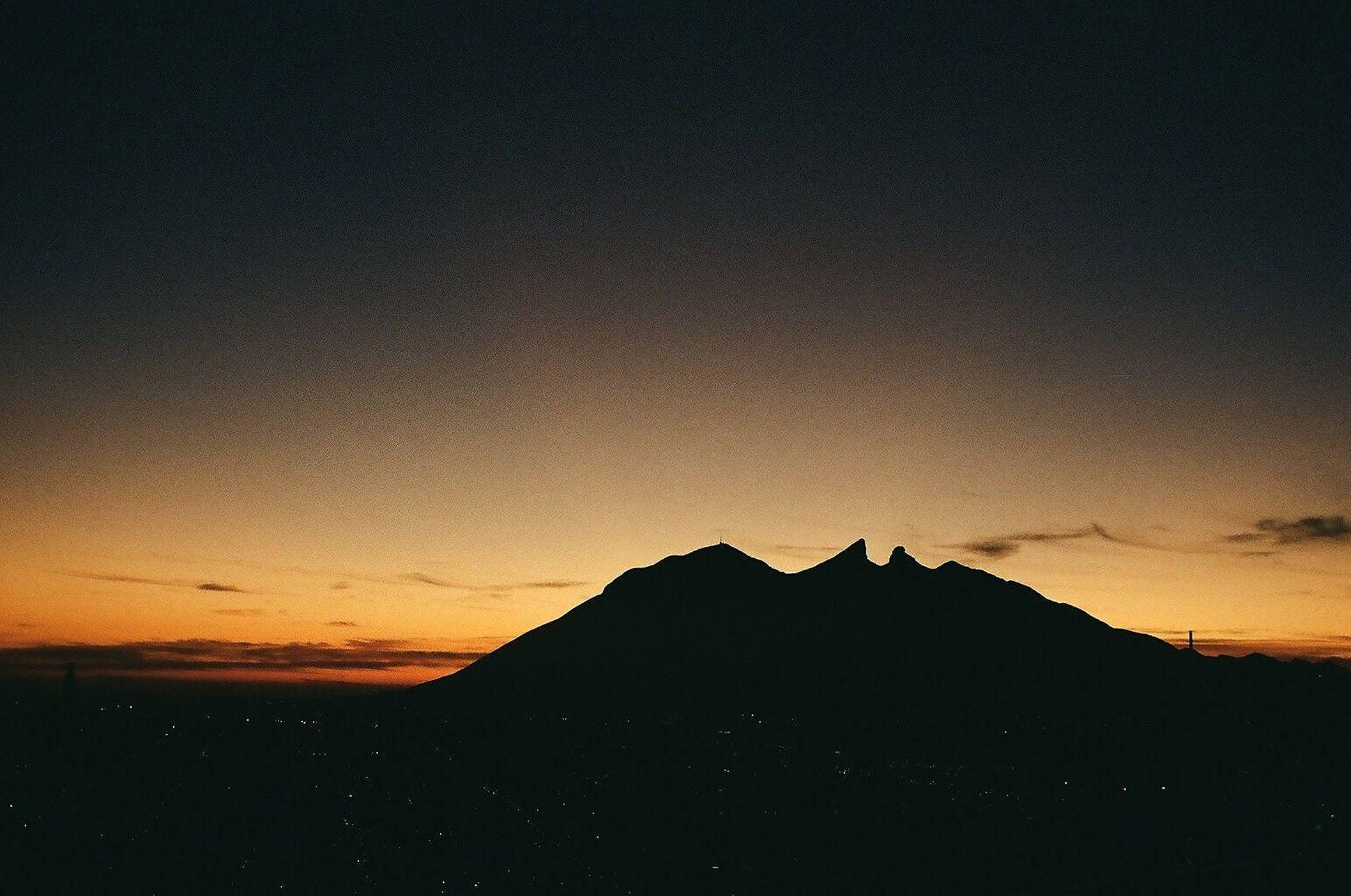 Monterrey 桌布 壁紙 — 鋸齒狀山峰的剪影，映襯著漸變的日落天空，散發橙色和深藍色光芒。