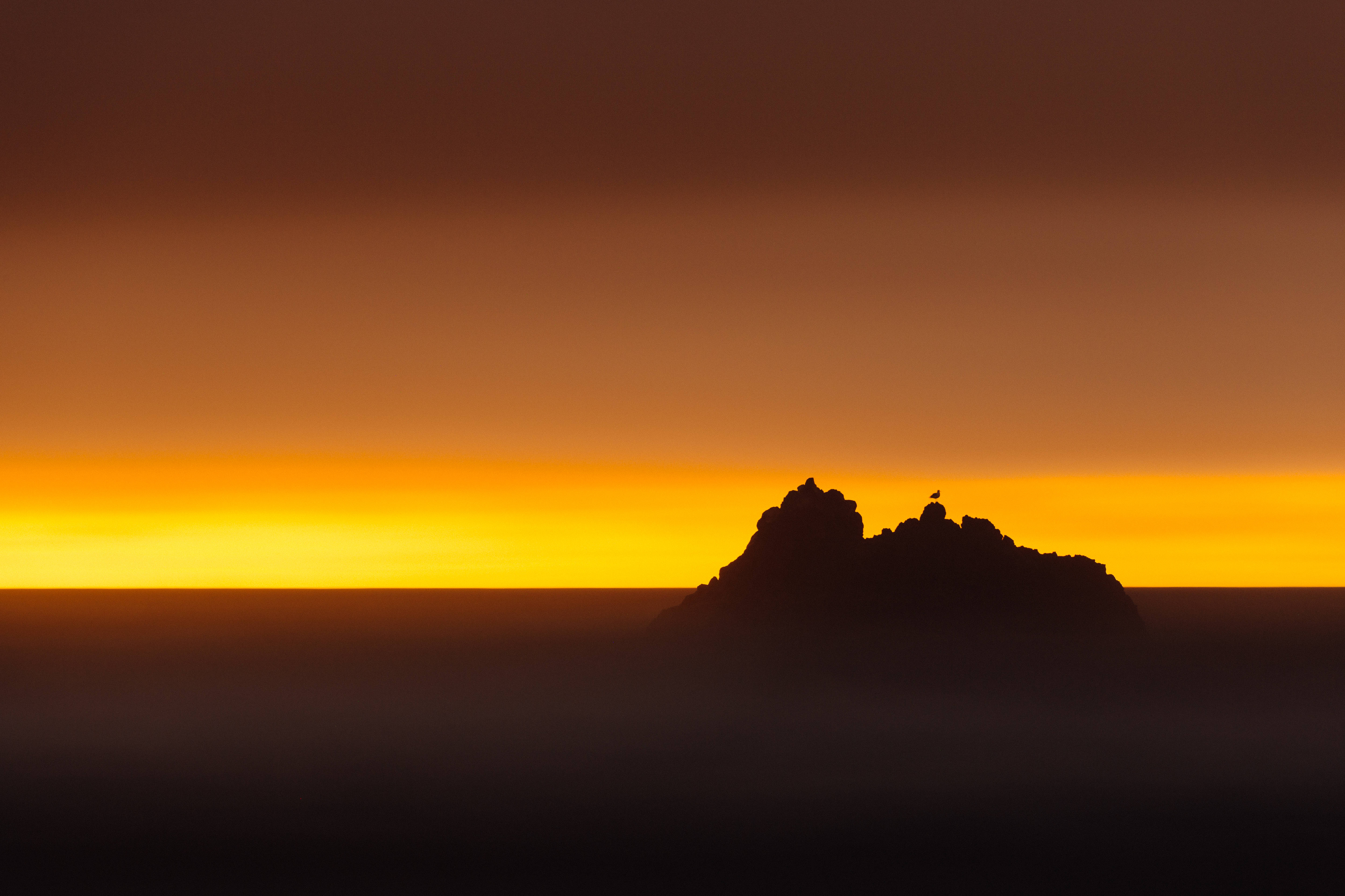 夕陽天空 桌布 壁紙 — 鋸齒狀岩石形成在霧海上空，以火紅橙黃色日落天空為背景，呈現黑色剪影。