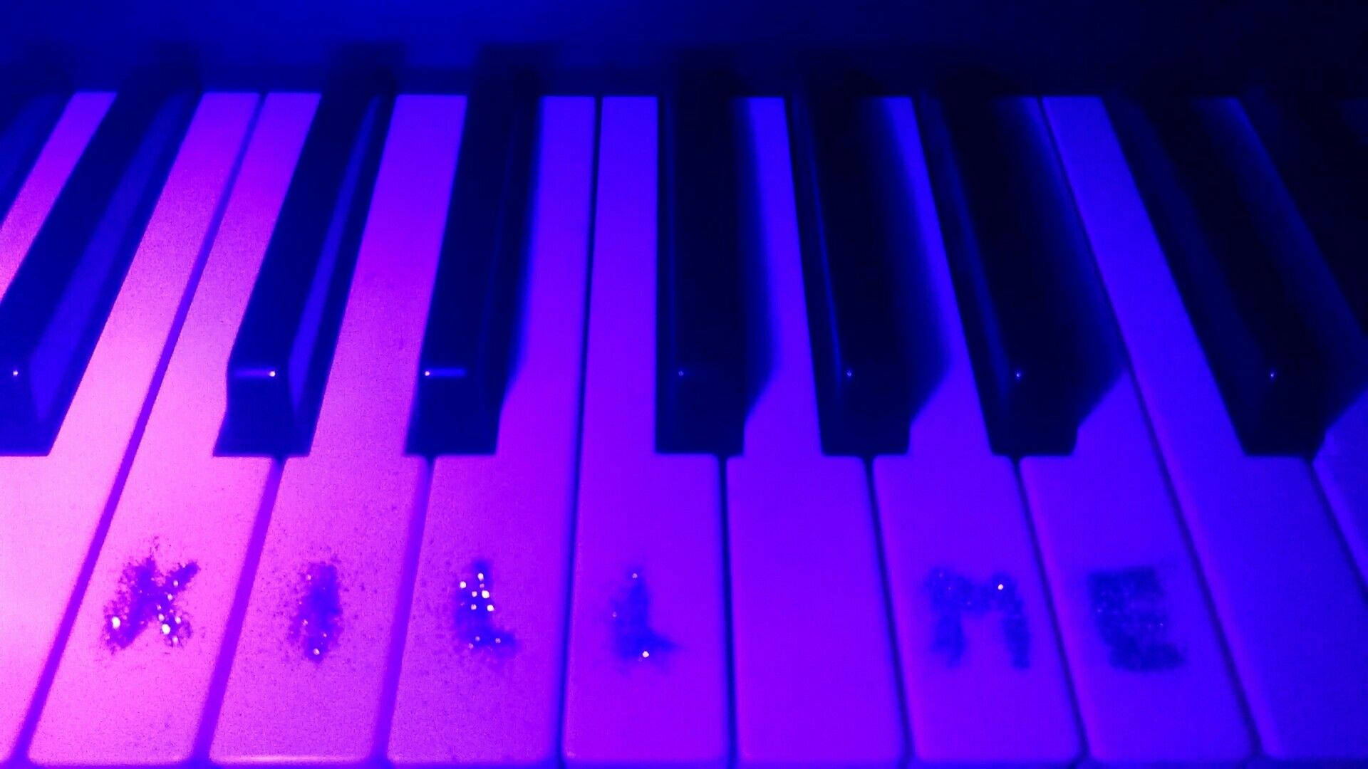 Piano 桌布 壁紙 — 鋼琴琴鍵在紫色和藍色燈光下發光的特寫，白色琴鍵上有亮粉拼出「KILL ME」。
