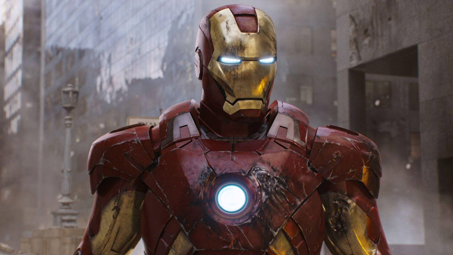 Iron Man Mark 3 桌布 壁紙 — 鋼鐵人因戰鬥而磨損的紅色和金色盔甲在煙霧瀰漫的城市廢墟背景下，發出明亮的胸部弧形反應器光芒。