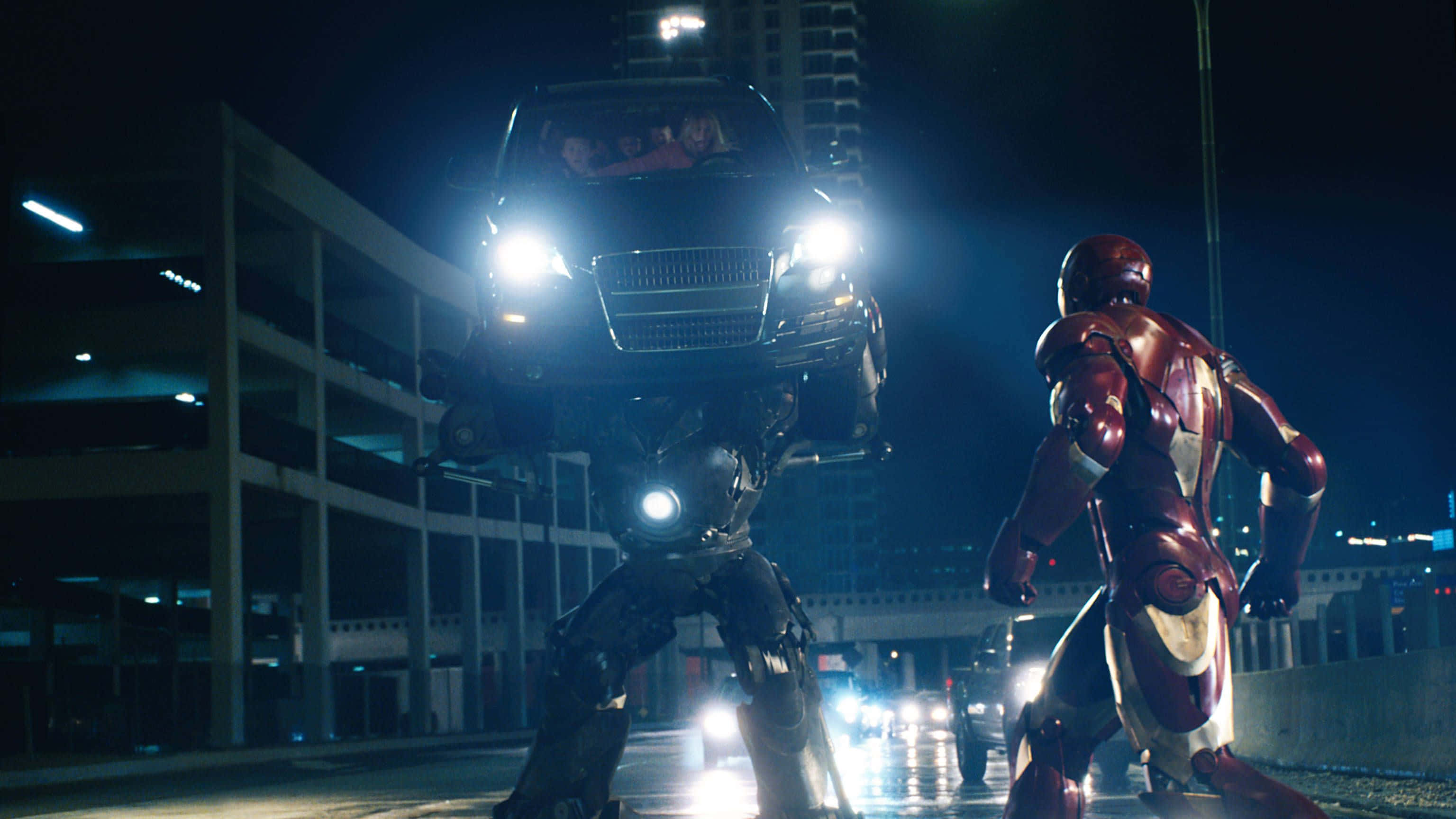 Iron Monger 桌布 壁紙 — 鋼鐵人在夜晚霓虹燈照亮的城市停車場中，面對一個拿著汽車的巨型機甲。