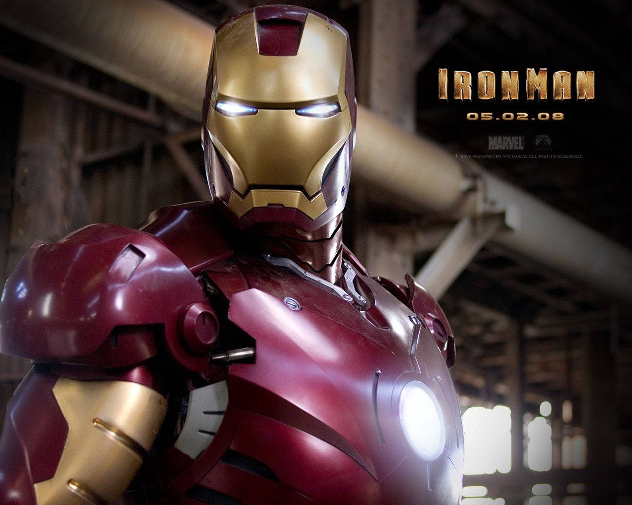 Iron Man Mark 3 桌布 壁紙 — 鋼鐵人穿著標誌性的紅色和金色戰衣，站在昏暗的工業機庫中，眼睛和胸部弧形反應爐發光。