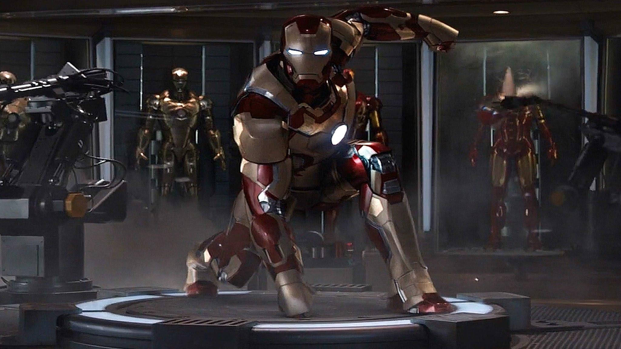 Iron Man Mark 3 桌布 壁紙 — 鋼鐵人穿著紅金色裝甲，蹲在一個高科技實驗室的圓形平台上，身後展示櫃中有其他戰衣。