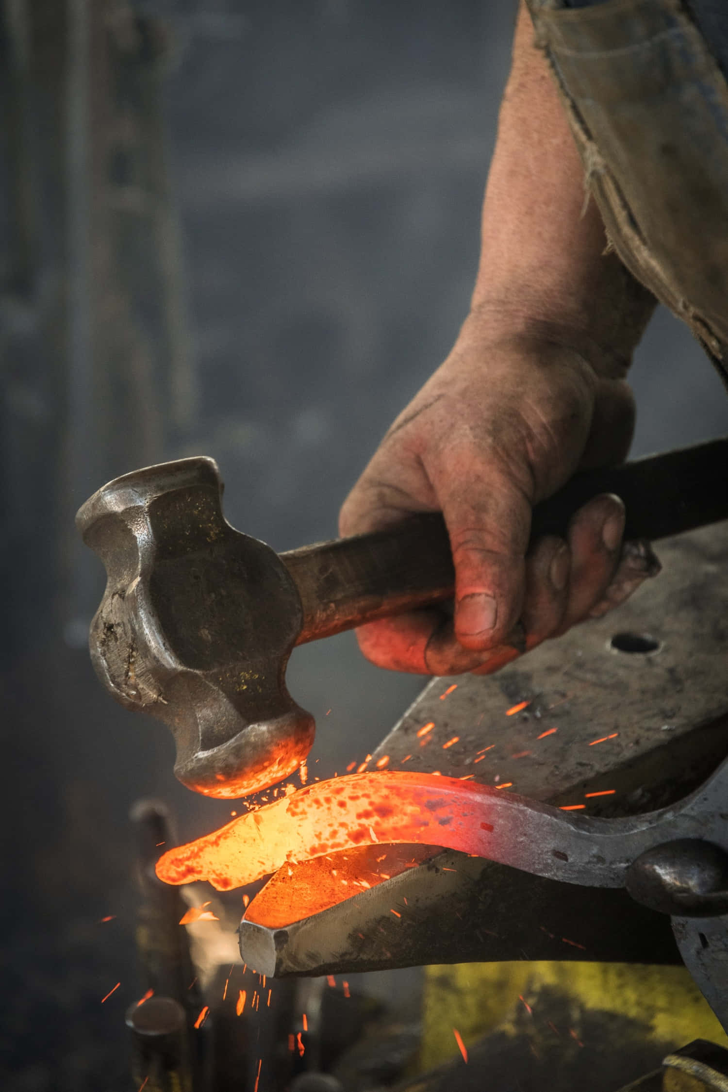 Blacksmith 桌布 壁紙 — 鐵匠的手在鐵砧上敲打一塊熾熱的橙色金屬片，在昏暗的工場中濺起火花。