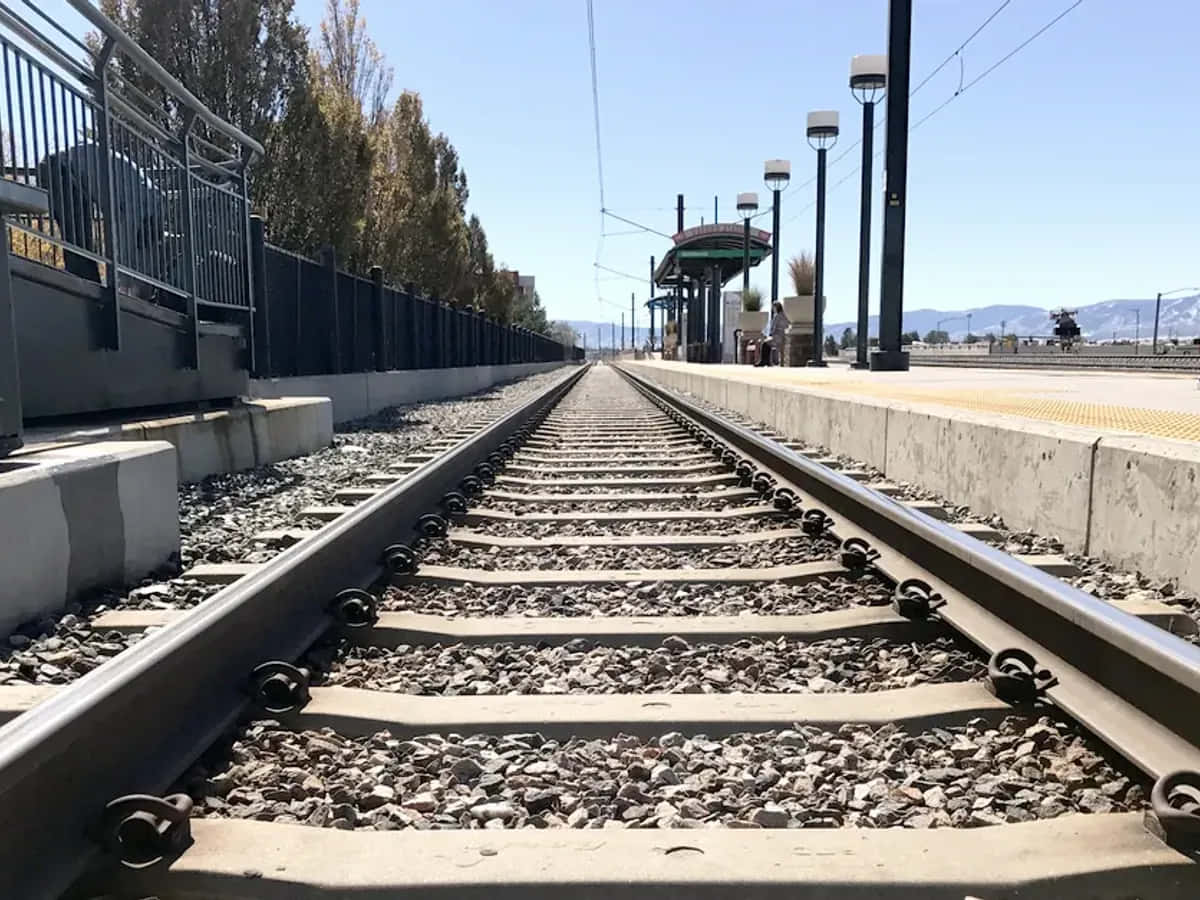 攝影 桌布 壁紙 — 鐵路軌道在晴朗的藍天下延伸至遠方，可見車站月台和遠處的山脈。
