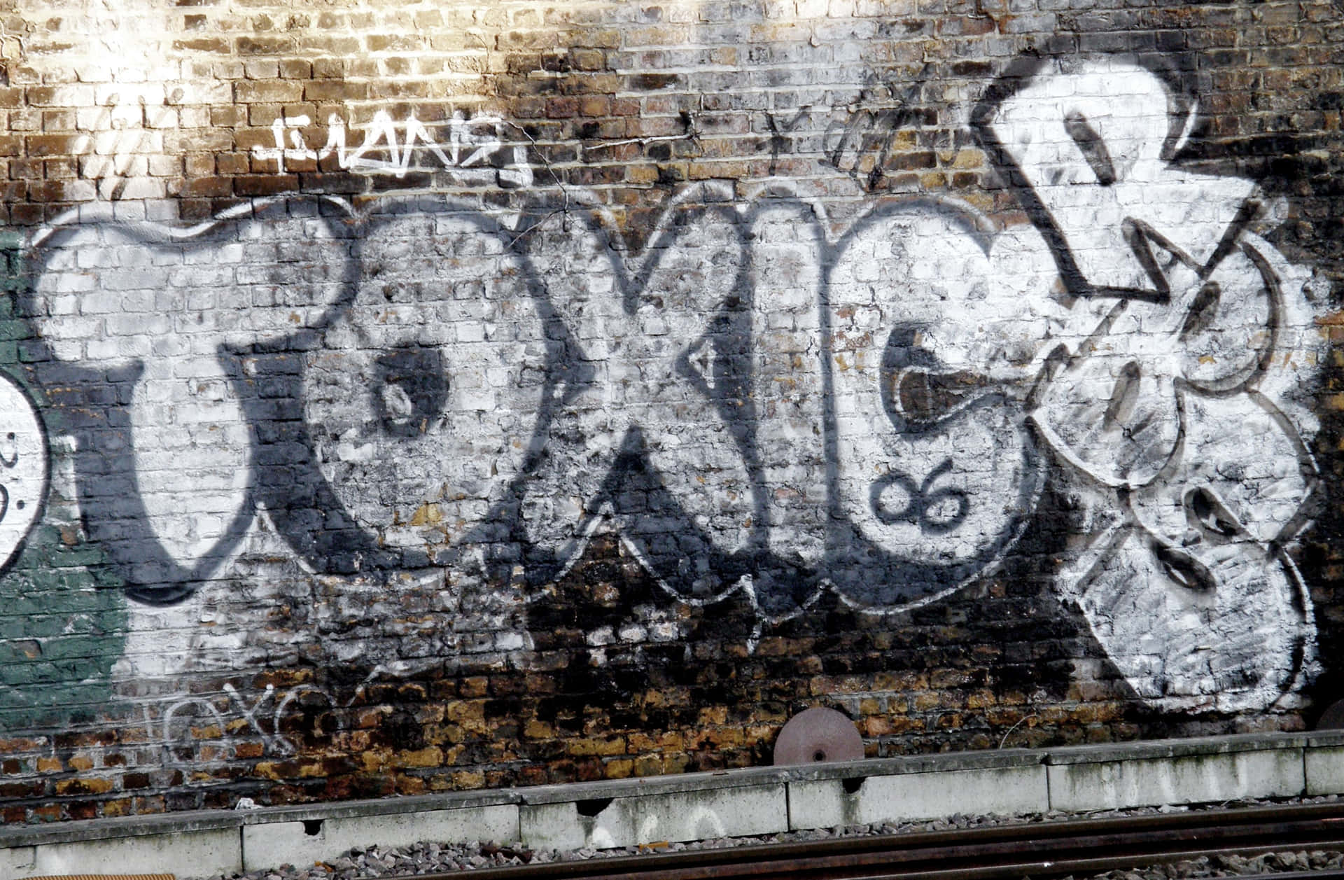 toxic 桌布 壁紙 — 鐵路軌道旁風化的磚牆上，粗體白色塗鴉 toxic 佔據主導地位。