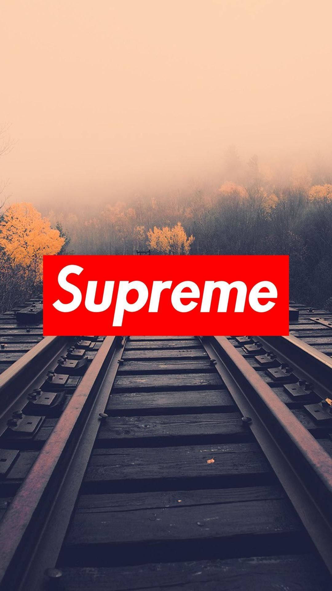supreme 桌布 壁紙 — 鐵路軌道消失在迷霧秋林中，朦朧的橙色天空下，中央有一個醒目的紅色Supreme標誌。
