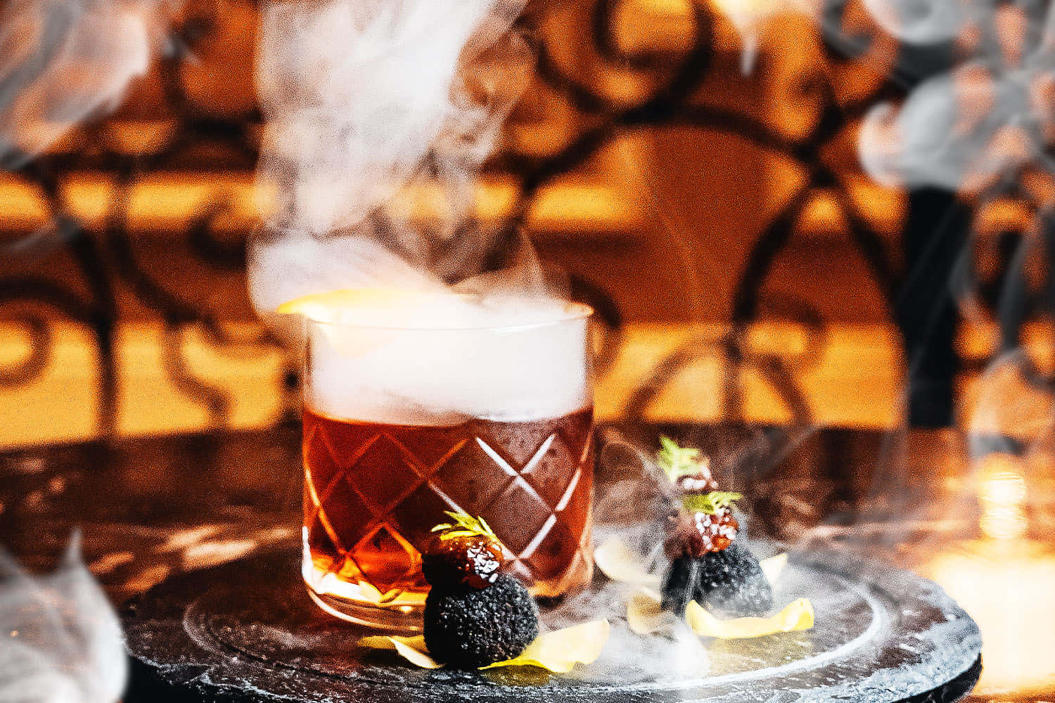 alcohol 桌布 壁紙 — 鑽石切割玻璃杯中的煙燻琥珀色雞尾酒在黑色松露和裝飾的深色石板托盤上戲劇性地冒著蒸汽。