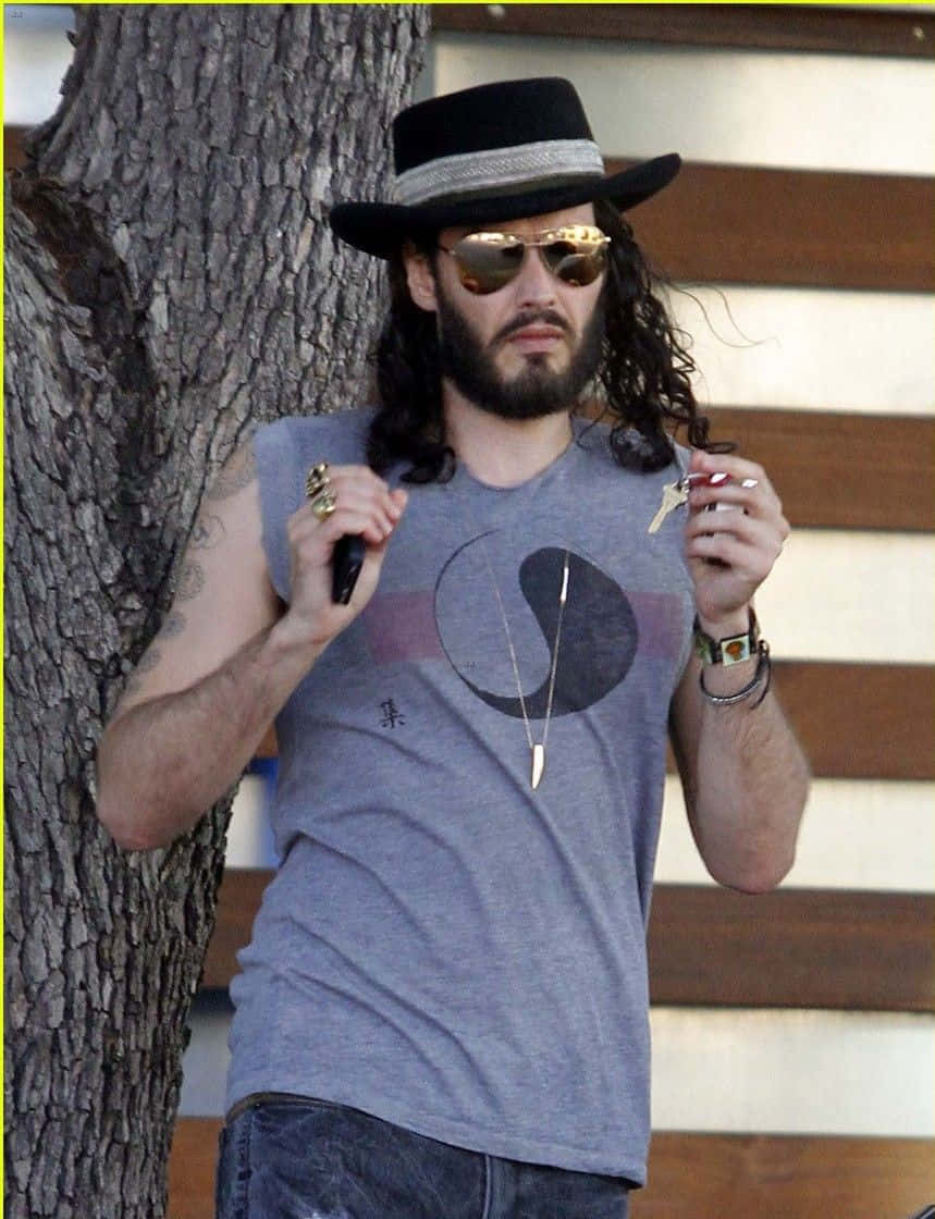 Celebrity 桌布 壁紙 — 長捲髮戴黑帽的男人靠著樹，手持鑰匙和手機。