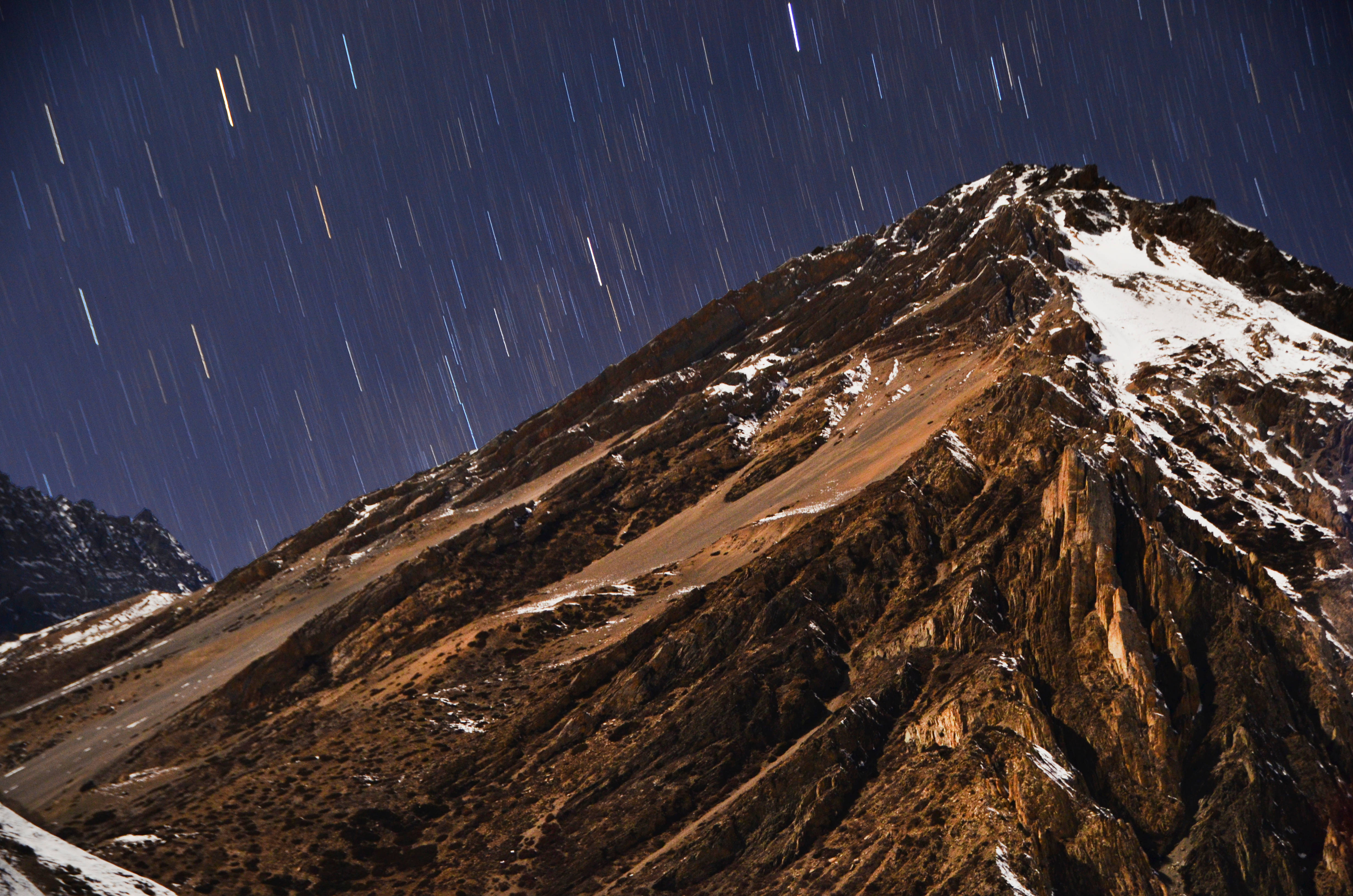 Nepal 桌布 壁紙 — 長時間曝光下，星軌在崎嶇積雪的山峰上空劃過黑暗的天空。
