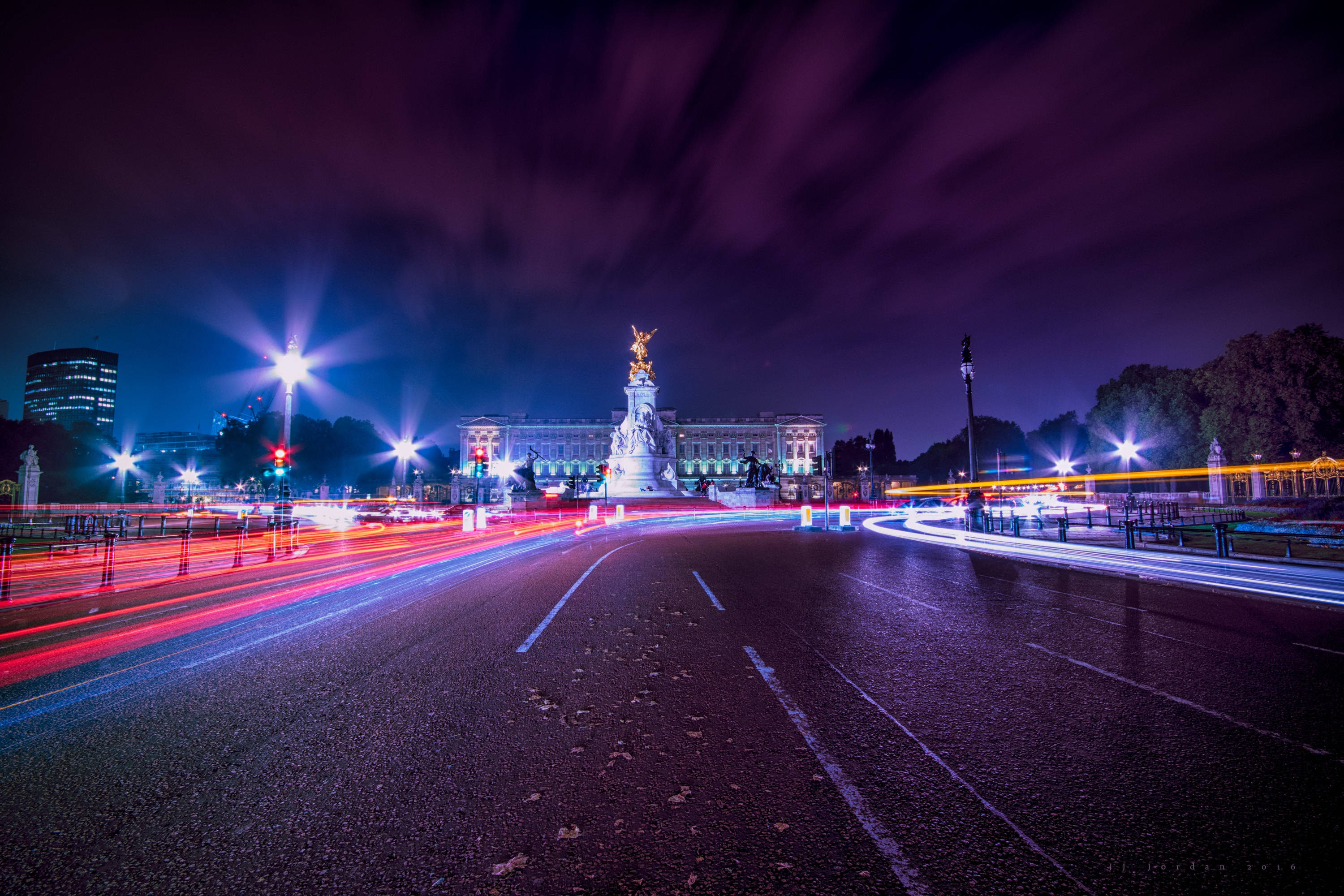 United Kingdom 桌布 壁紙 — 長時間曝光夜景捕捉到在深紫色天空下，汽車燈光疾馳掠過白金漢宮的鮮豔光軌。