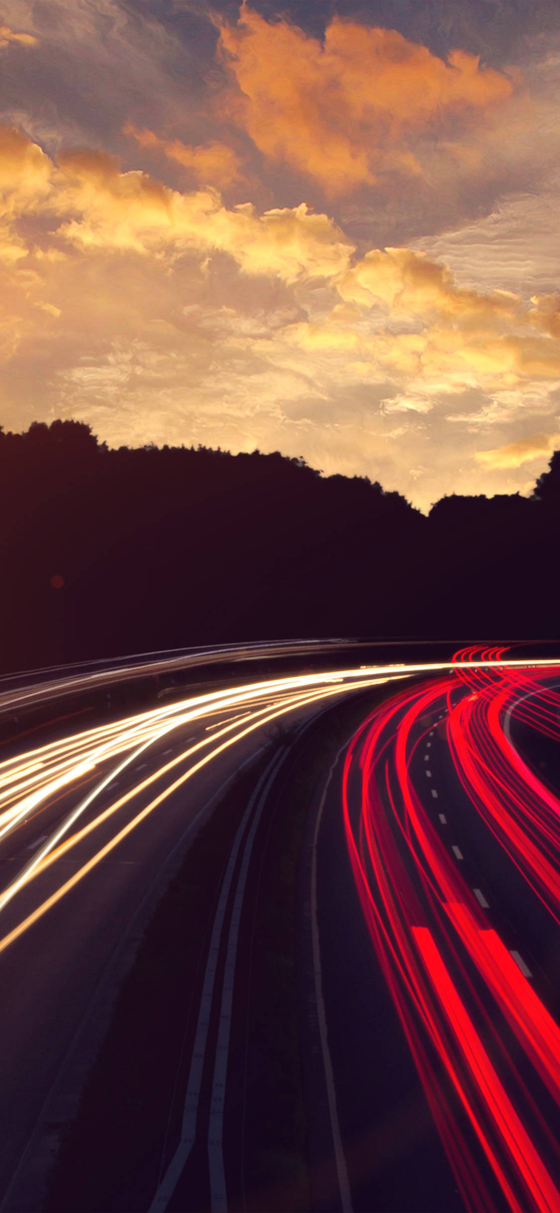 driving fast 桌布 壁紙 — 長時間曝光捕捉到在熾熱的日落天空下，沿著彎曲高速公路飛馳的汽車發出熾熱的紅色和白色光軌。