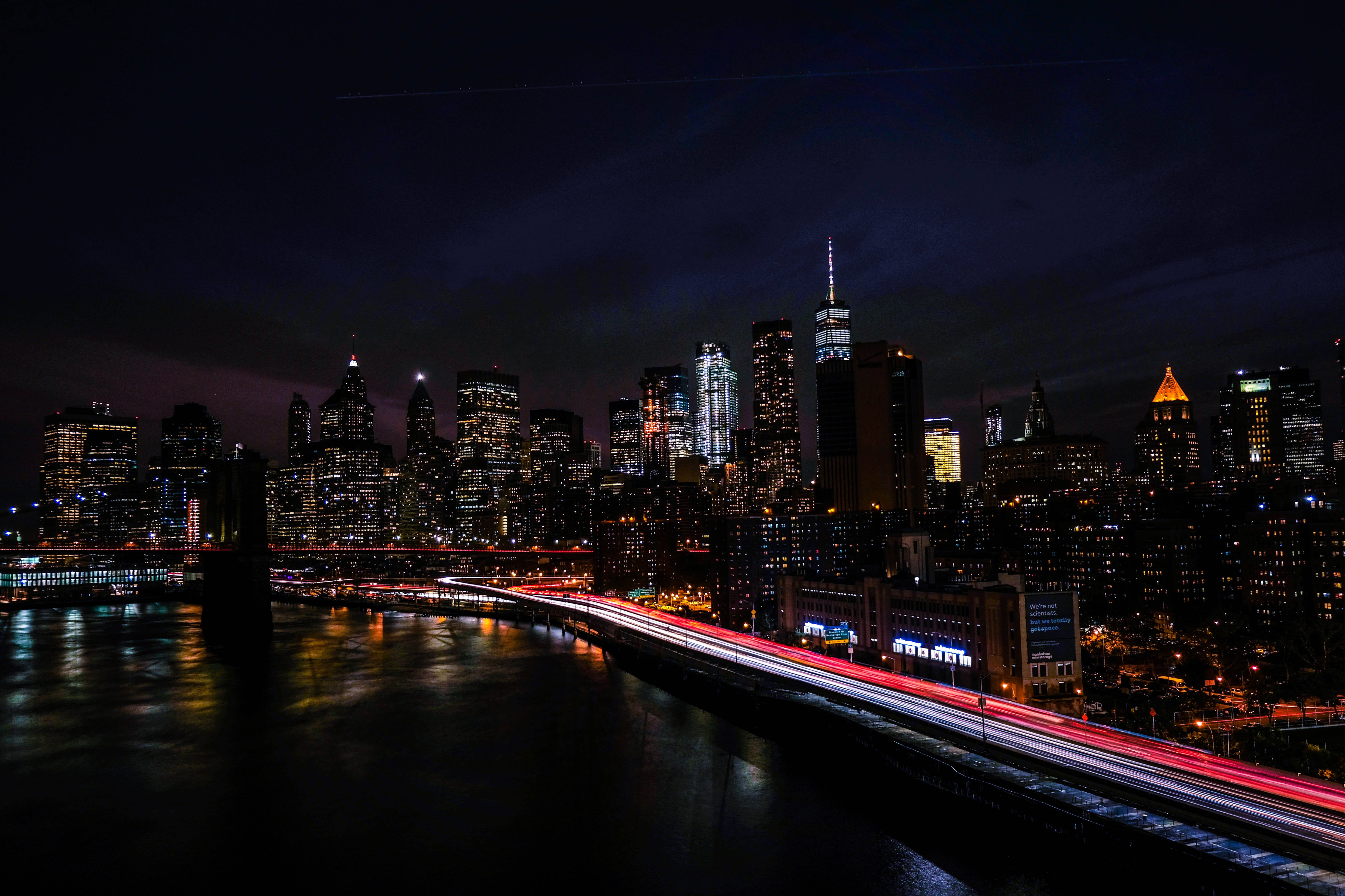 4K New York City 桌布 壁紙 — 長時間曝光捕捉到橋上交通的紅色和白色光線條紋，背景是閃爍的夜間城市天際線。