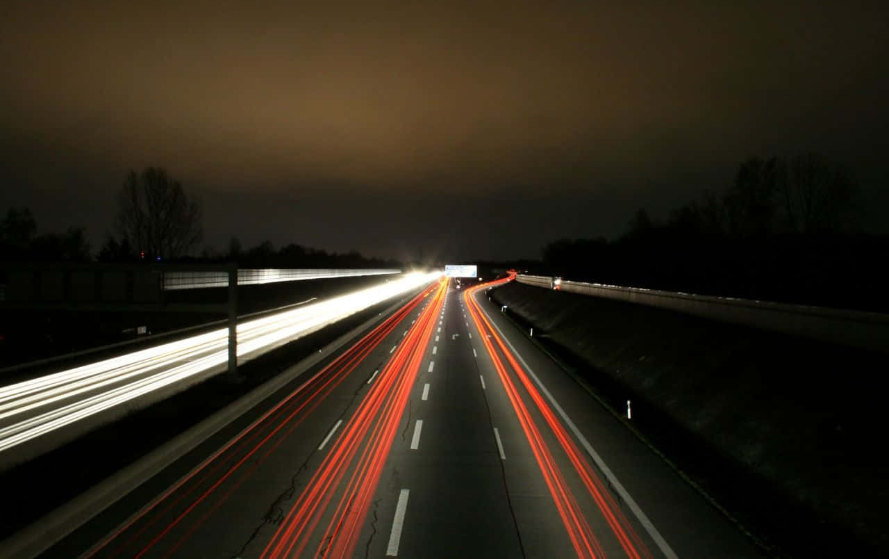 highway 桌布 壁紙 — 長時間曝光捕捉到白色和紅色車燈在夜間黑暗高速公路上飛馳的光軌。