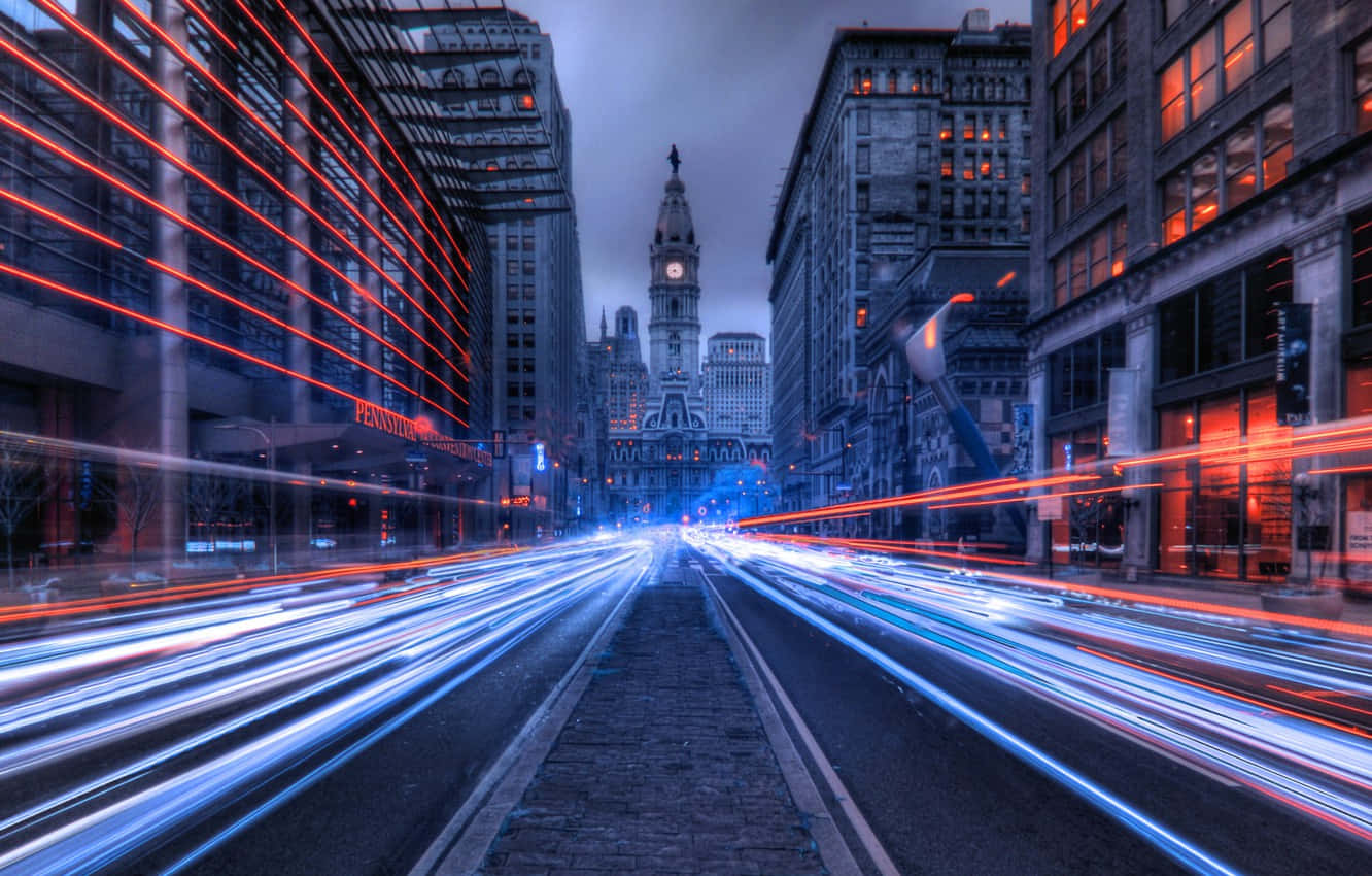 Philly 桌布 壁紙 — 長時間曝光捕捉到紅色和藍色光線穿過雨中的城市街道，奔向一座歷史悠久的鐘樓。